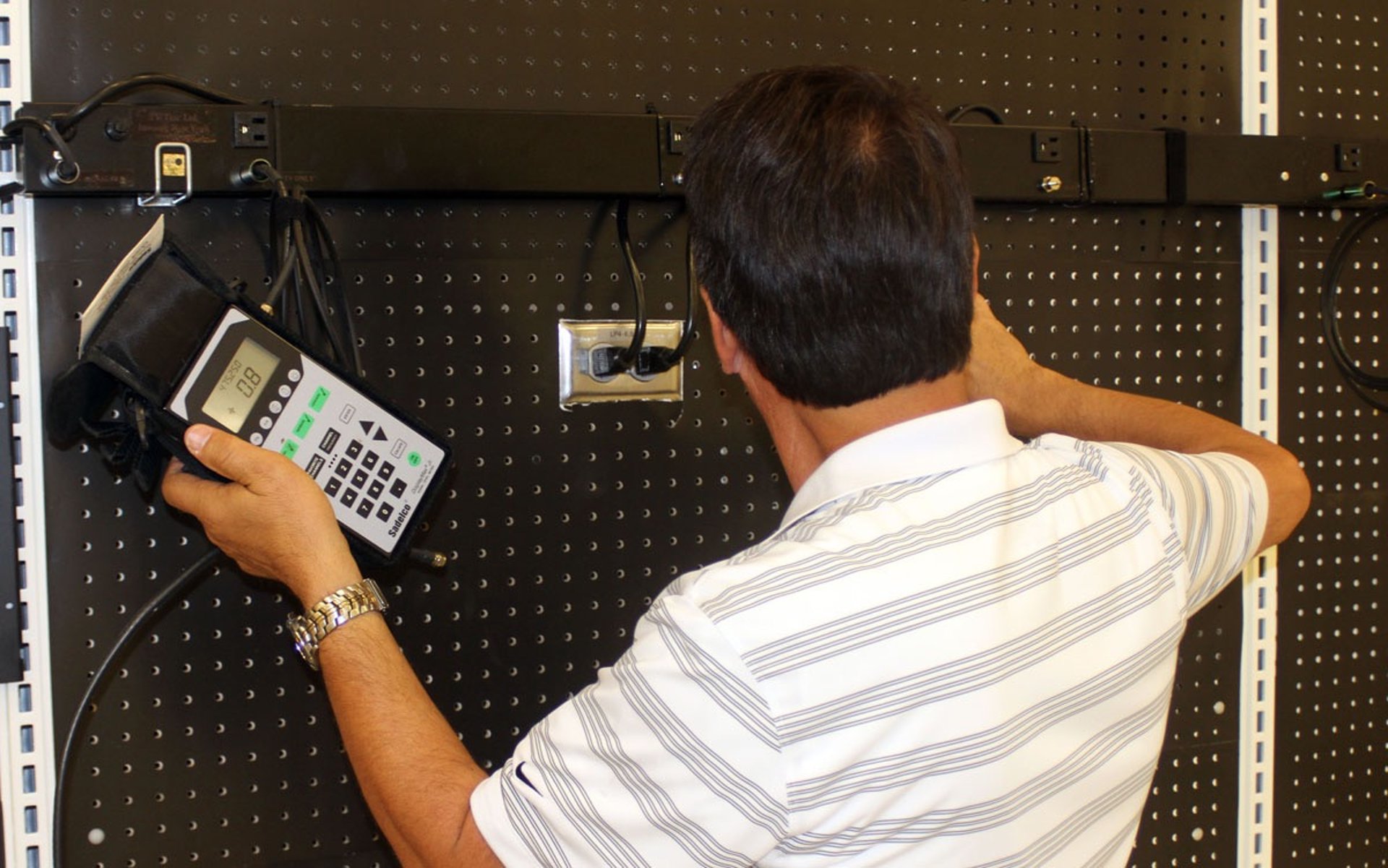 Technician using a handheld device to test a wall-mounted network port.
