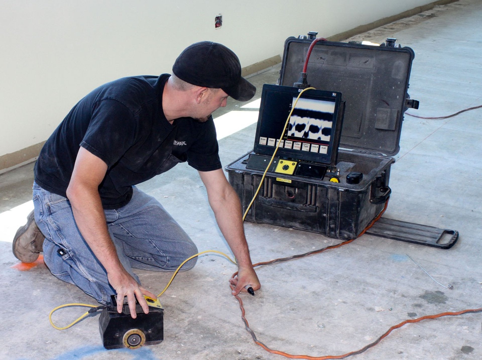 A technician kneels on the floor using specialized testing equipment for wiring.