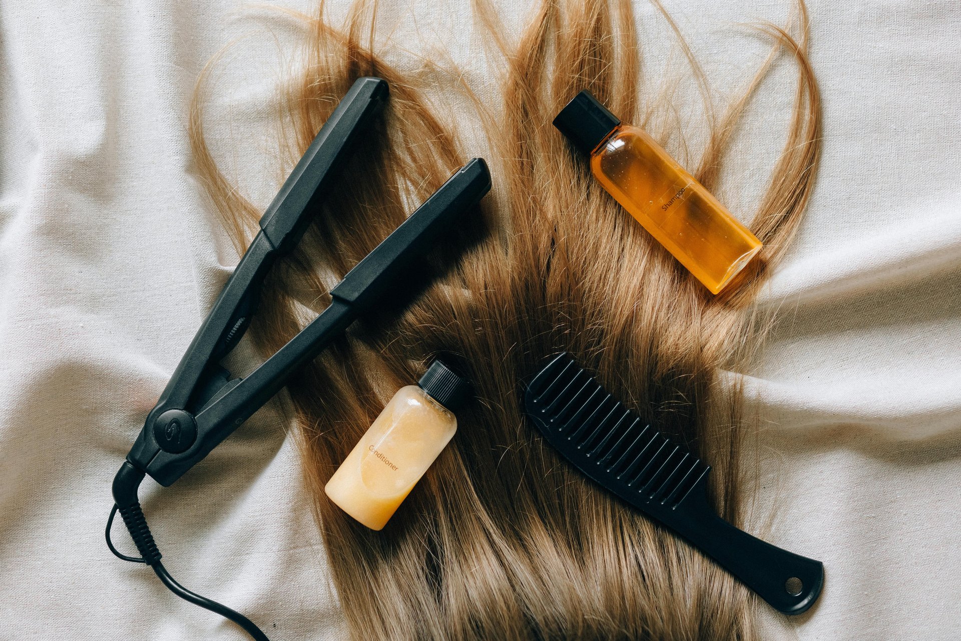 Plancha para el cabello, peine y botellas de shampoo tamaño de viaje sobre cabello.