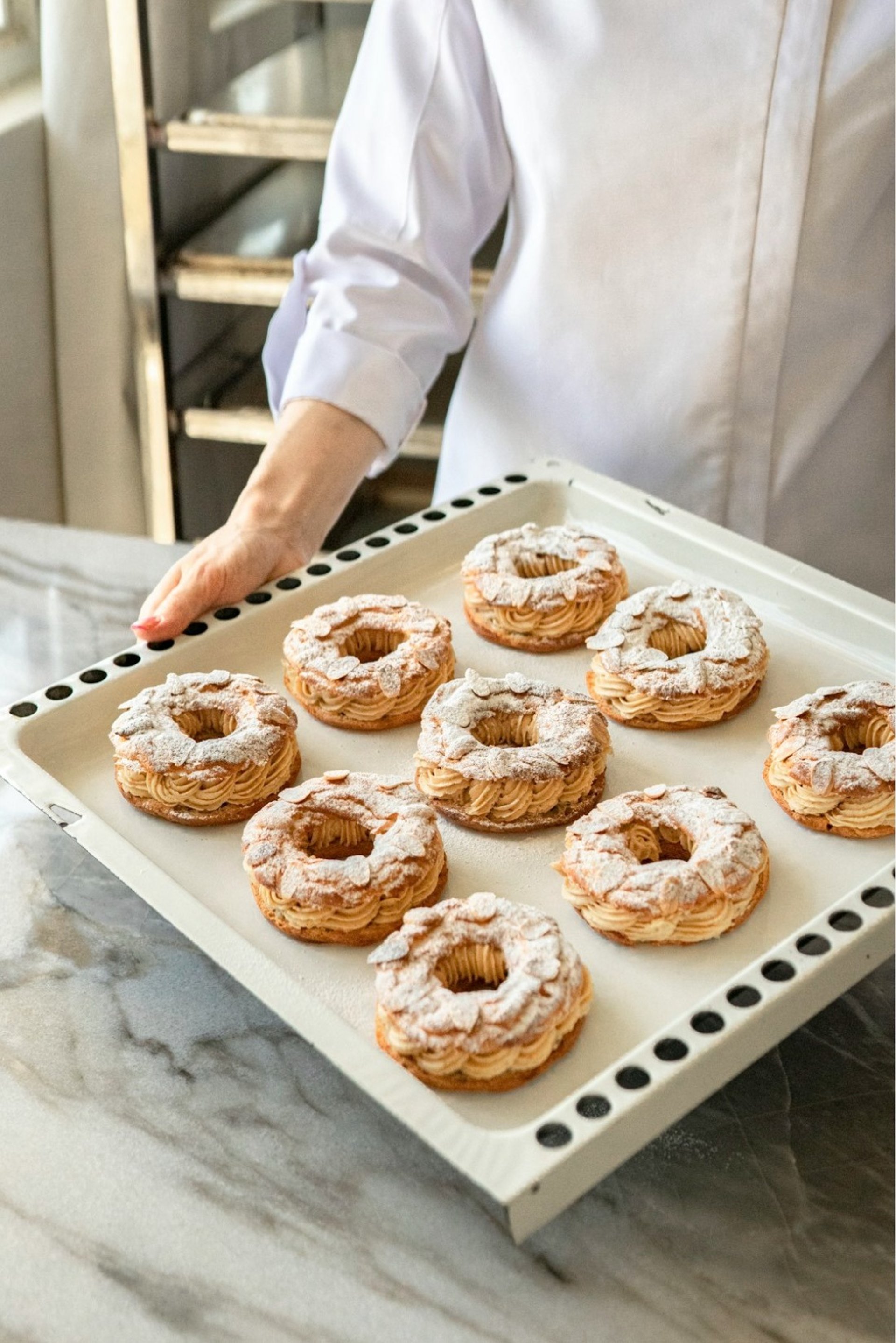 Baker holding tray of cream-filled pastries with almond pastries