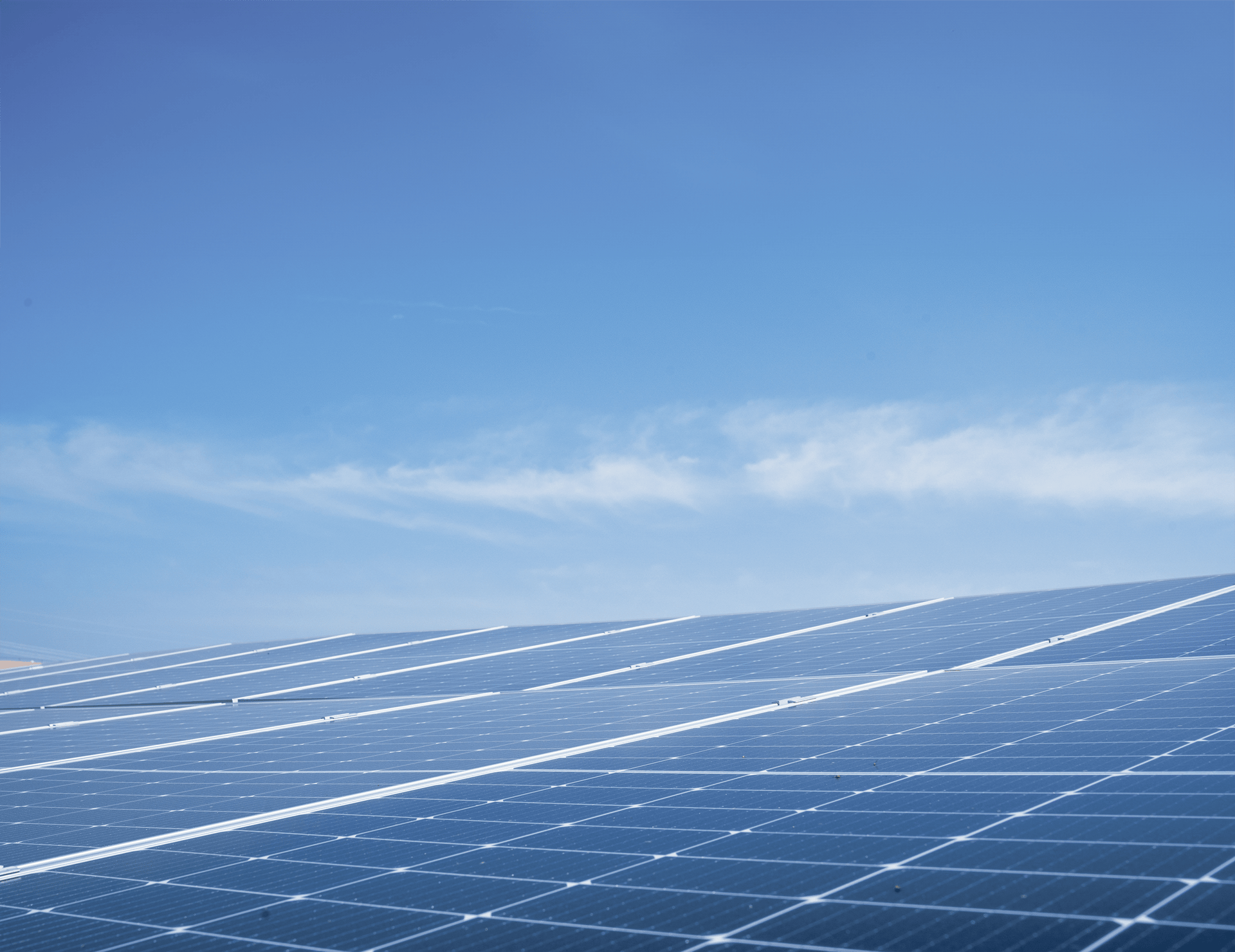 A close-up, low-angle view of several blue solar panels under a clear, bright blue sky with light wispy clouds
