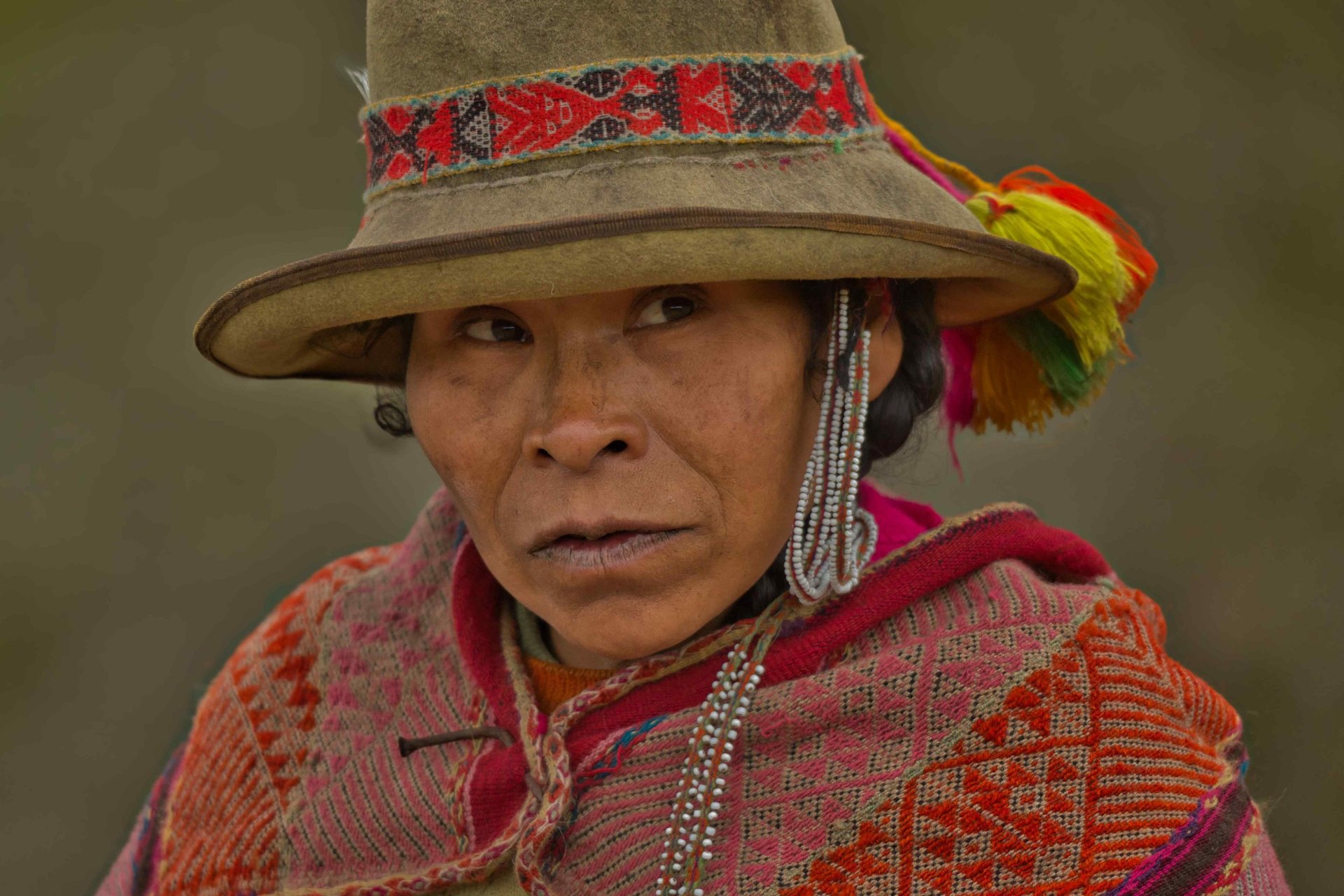 This image shows a person of Andean heritage wearing a traditional red felt hat called a montera.