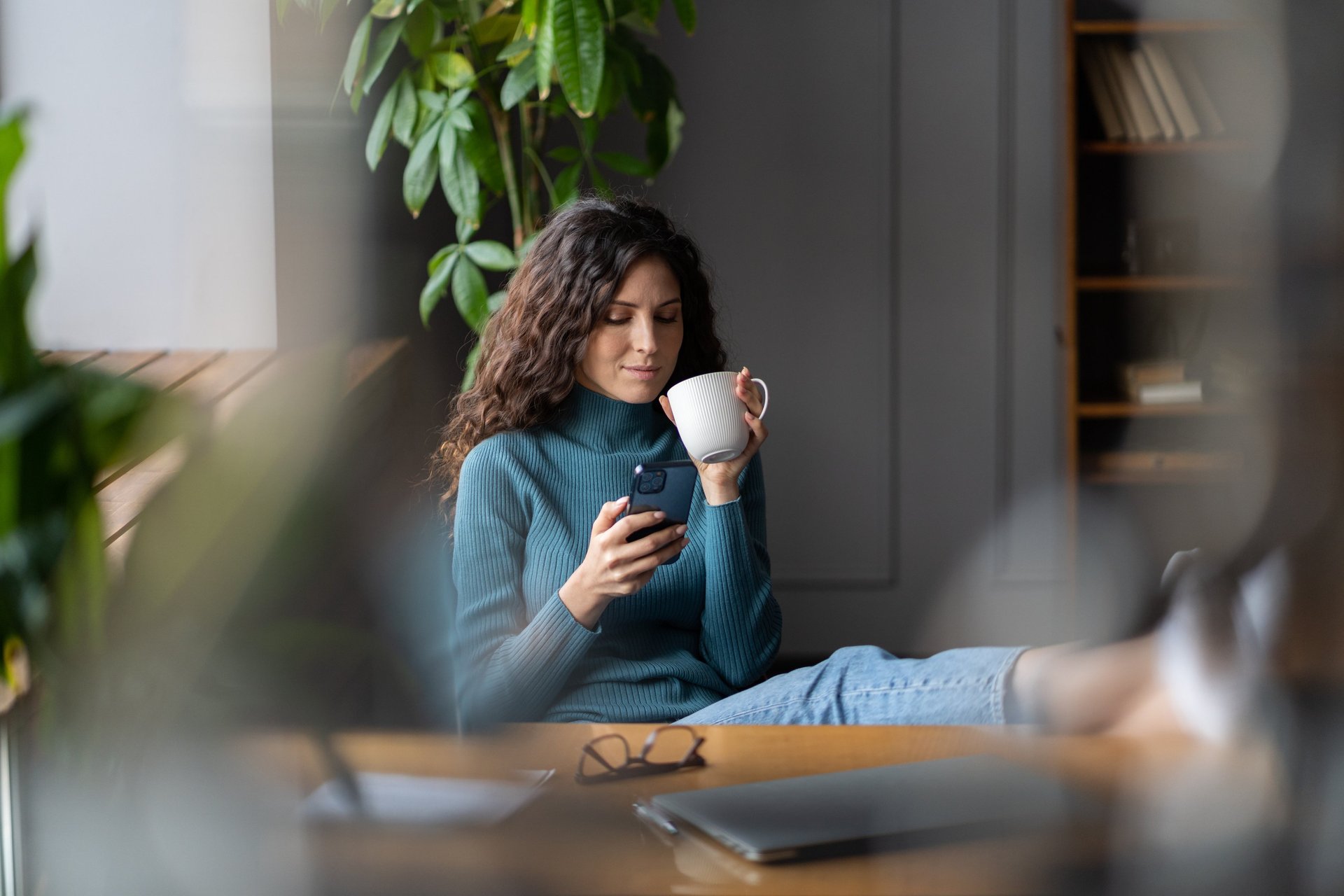A woman is drinking coffee and looking at her phone.
