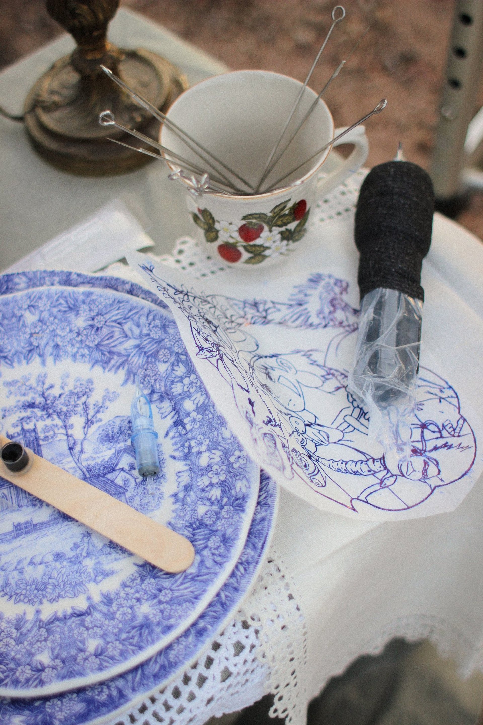 gros plan sur une assiette vintage, des aiguilles de tatouage, un calque de tattoo, un dermographe, sur une table à la nappe