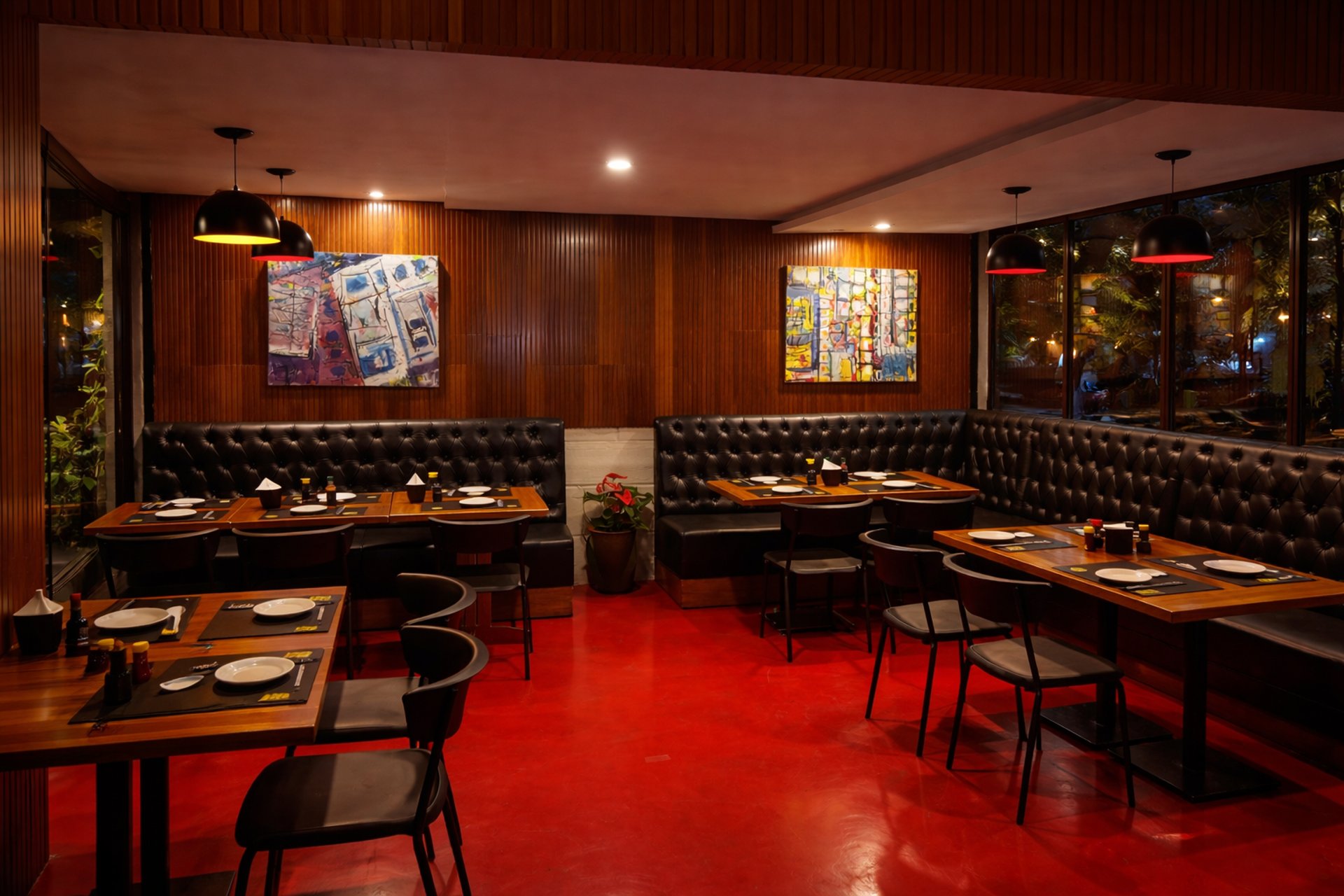 Interior do Okone SP com sofás pretos, mesas de madeira, piso vermelho e iluminação moderna