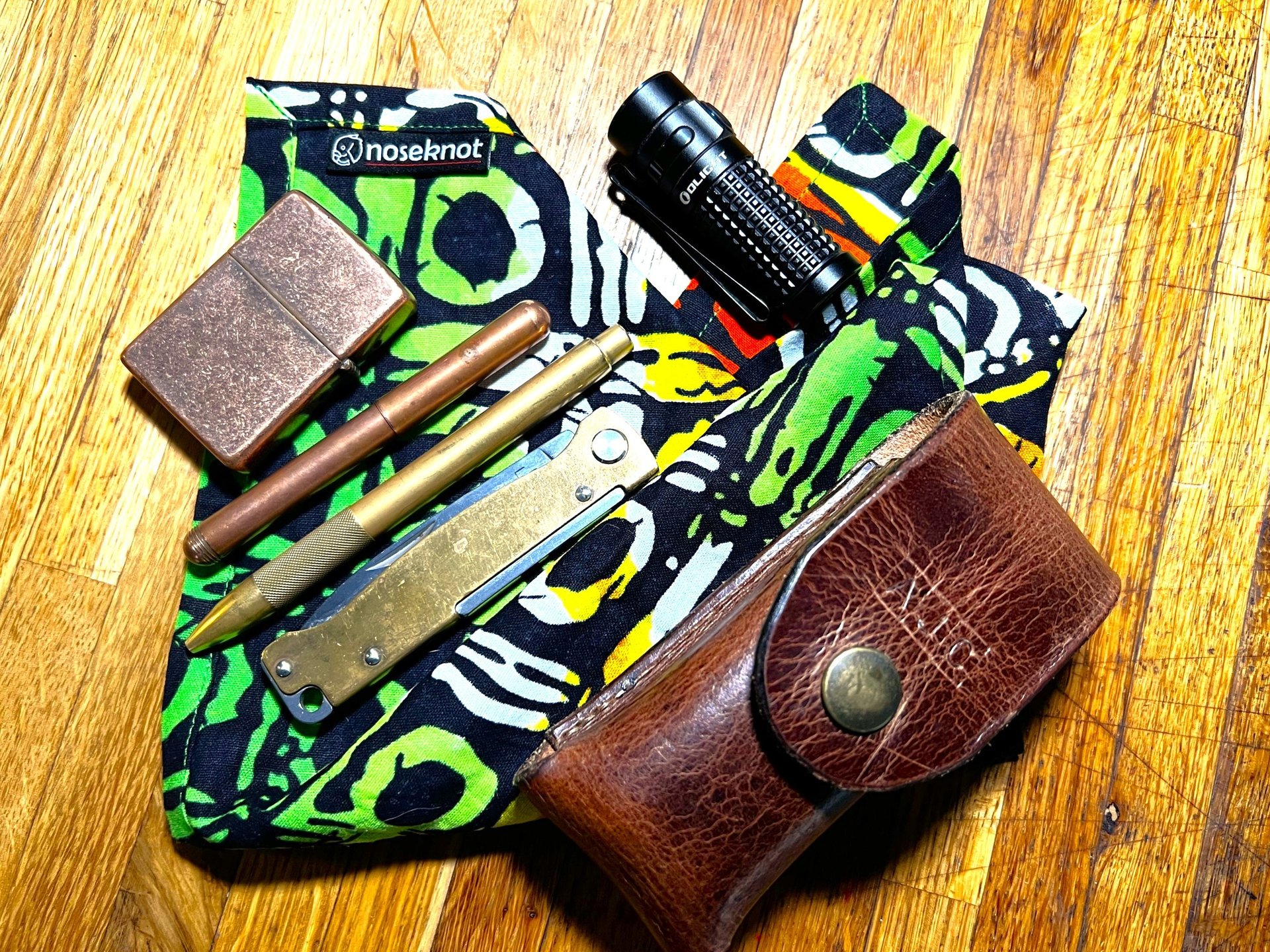 A noseknot handkerchief with a torch, lighter, brass pen, copper pencil. brass knife and a leather leatherman case