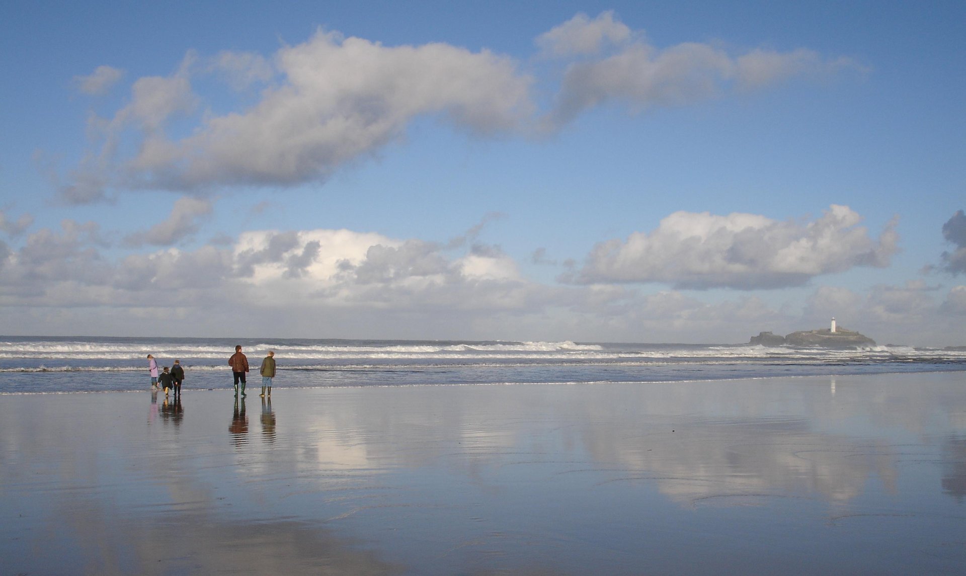 A family walking along a Cornish beach towards Godrevy Lighthouse