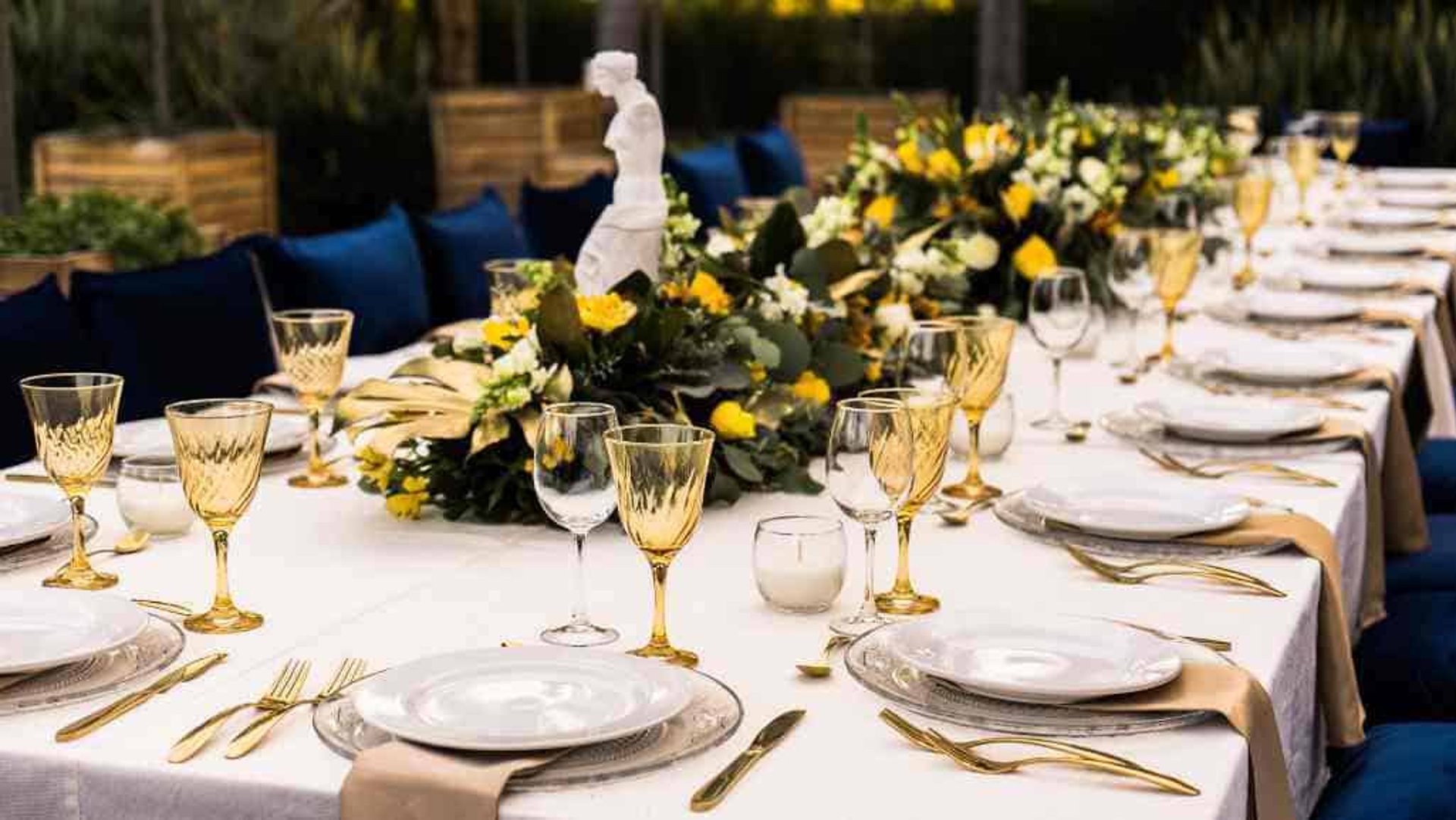 mesa montada para evento en colores amarillo, azul y blanco con camino de arreglo floral