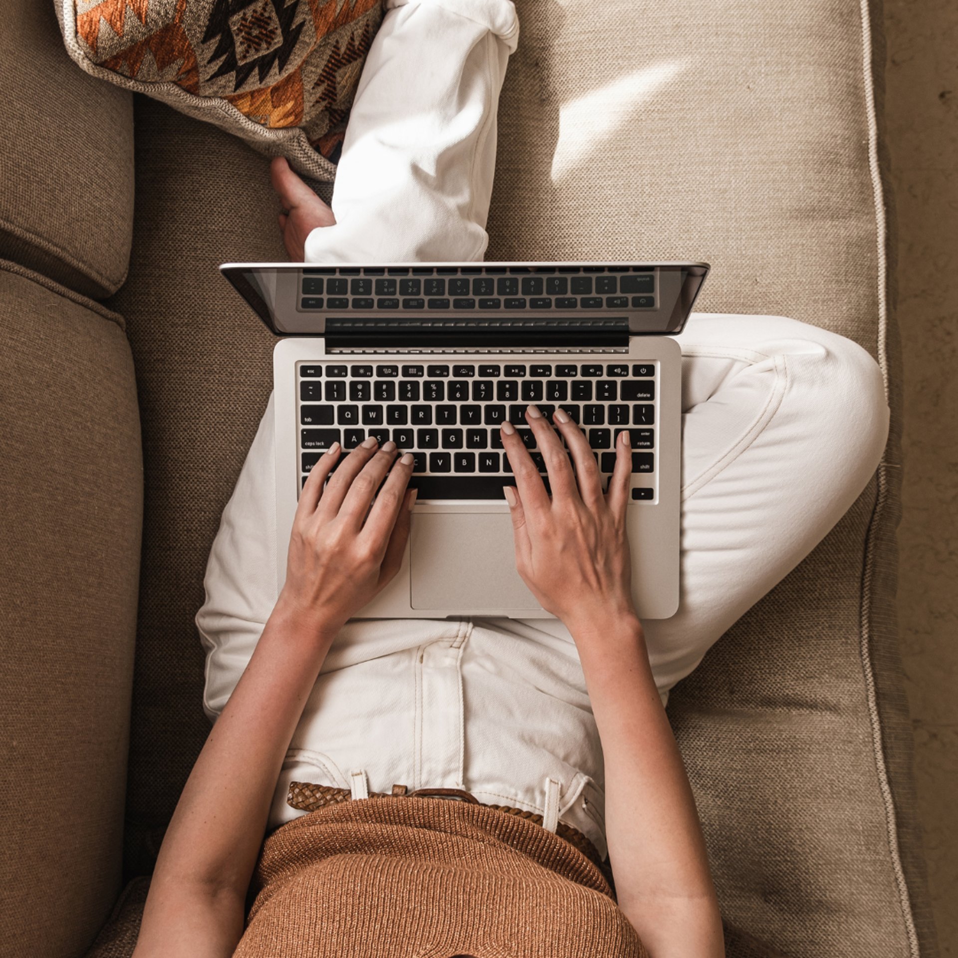 woman in white and black striped dress shirt sitting on floor in front of table while using laptop computer