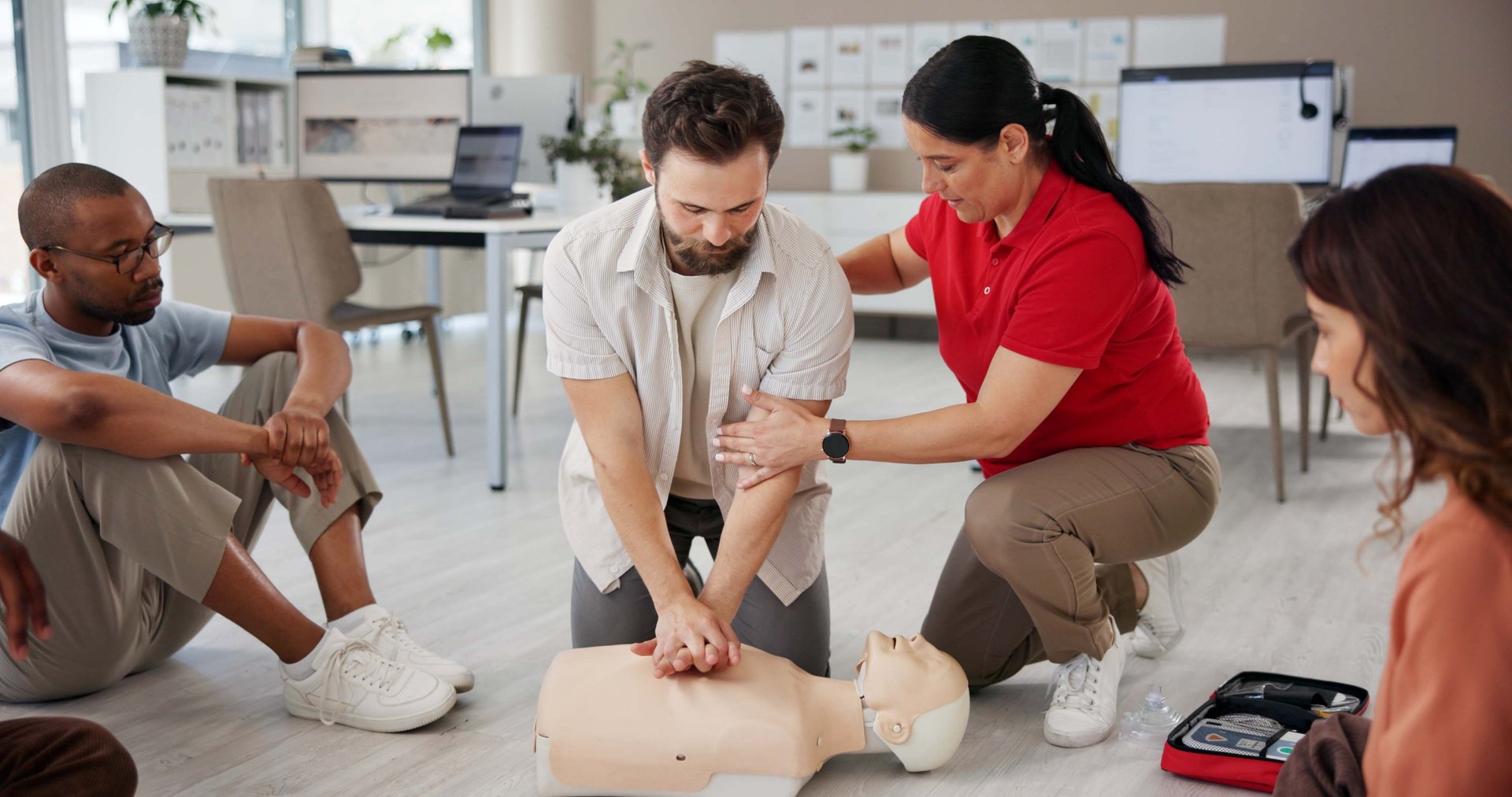 Female instructor assisting a male student learning how to perform CPR on a training mannequin