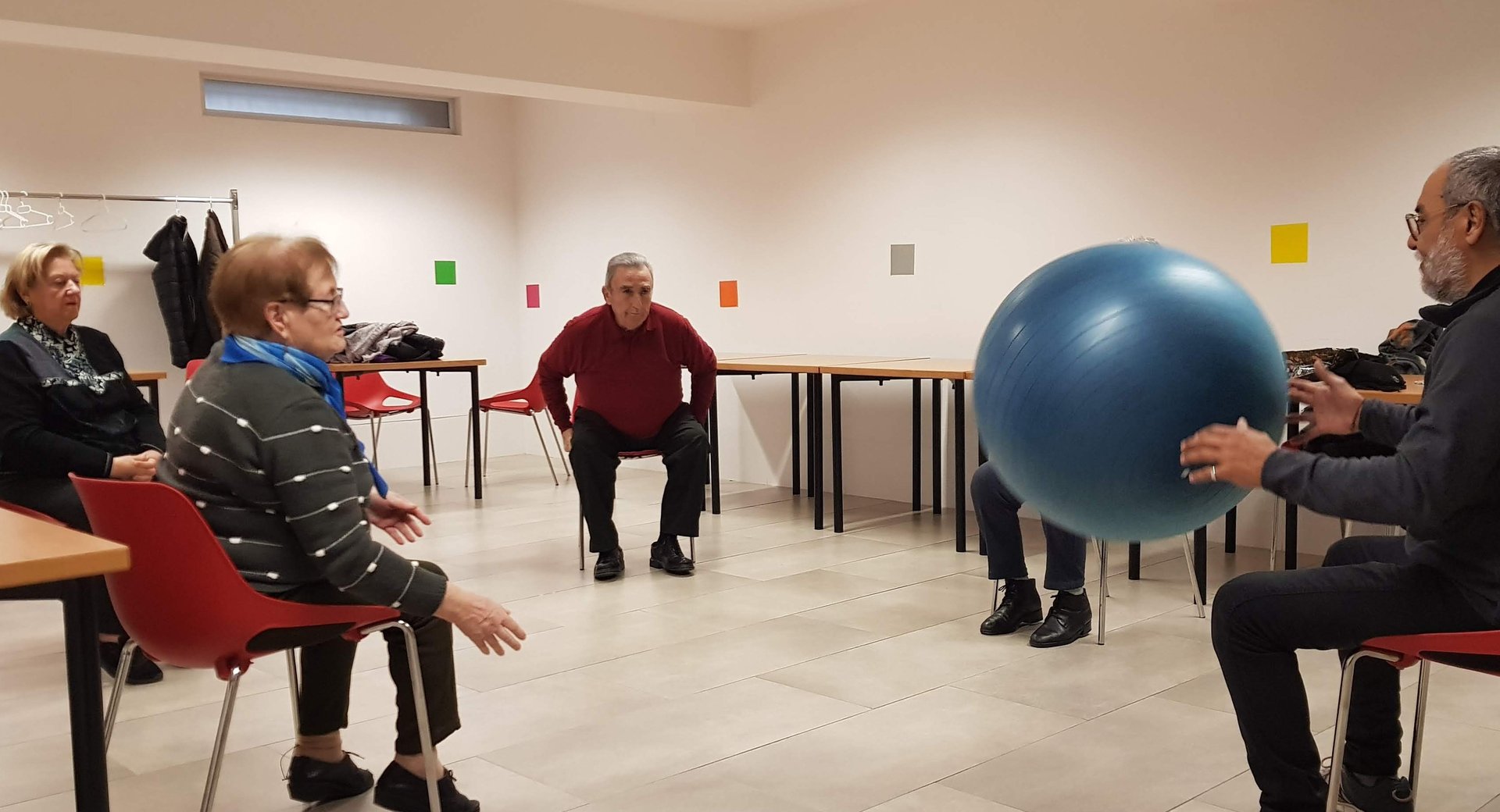 Un grupo de personas mayores está sentado en círculo realizando ejercicios con una pelota como parte