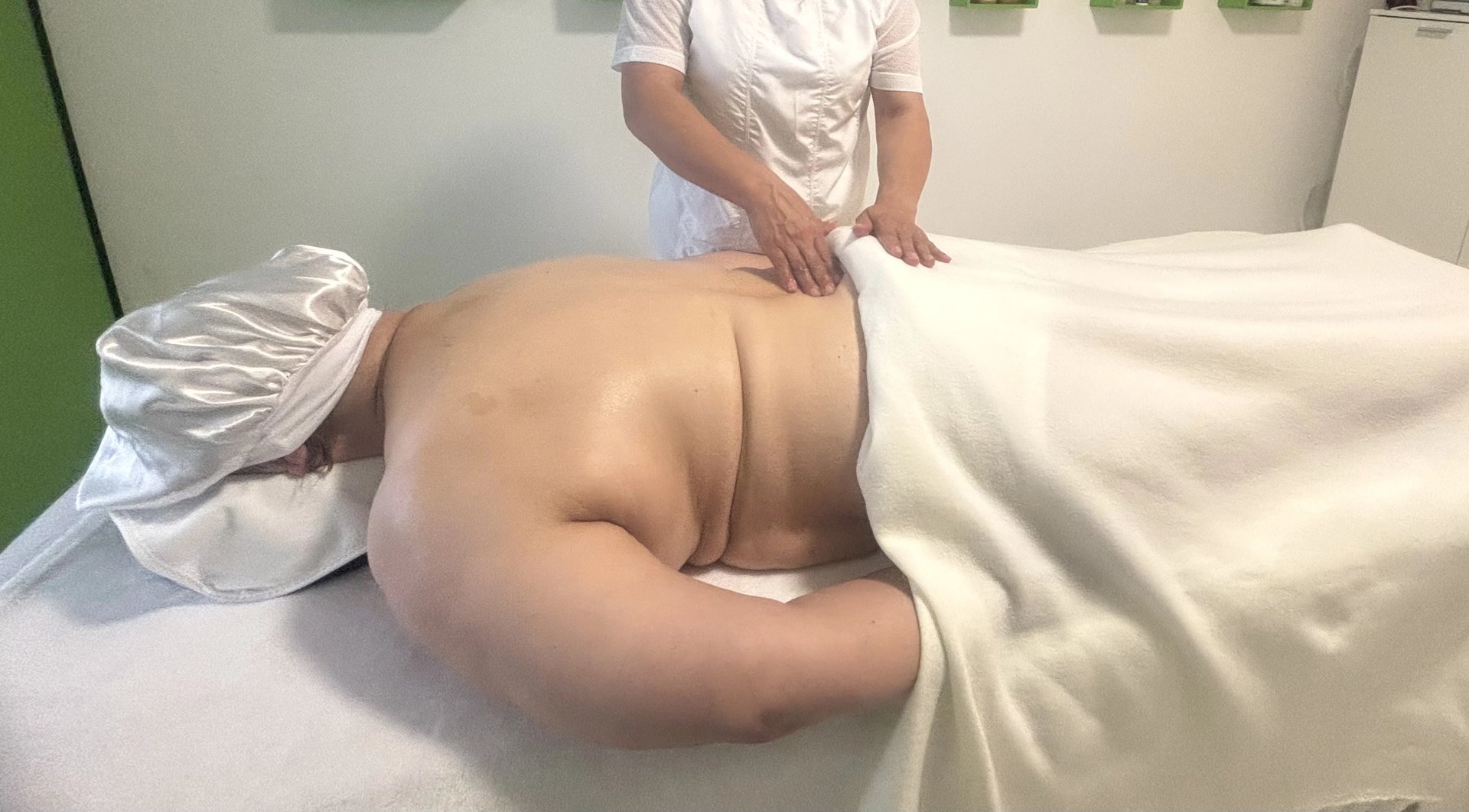Wellness-Massage: Eine Masseurin massiert den Rücken einer liegenden Person.
