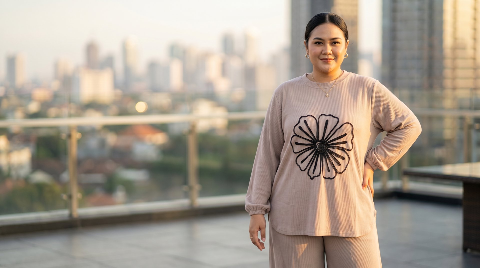 Plus-size woman in a beige floral sweatshirt posing on an urban rooftop with a city skyline view.