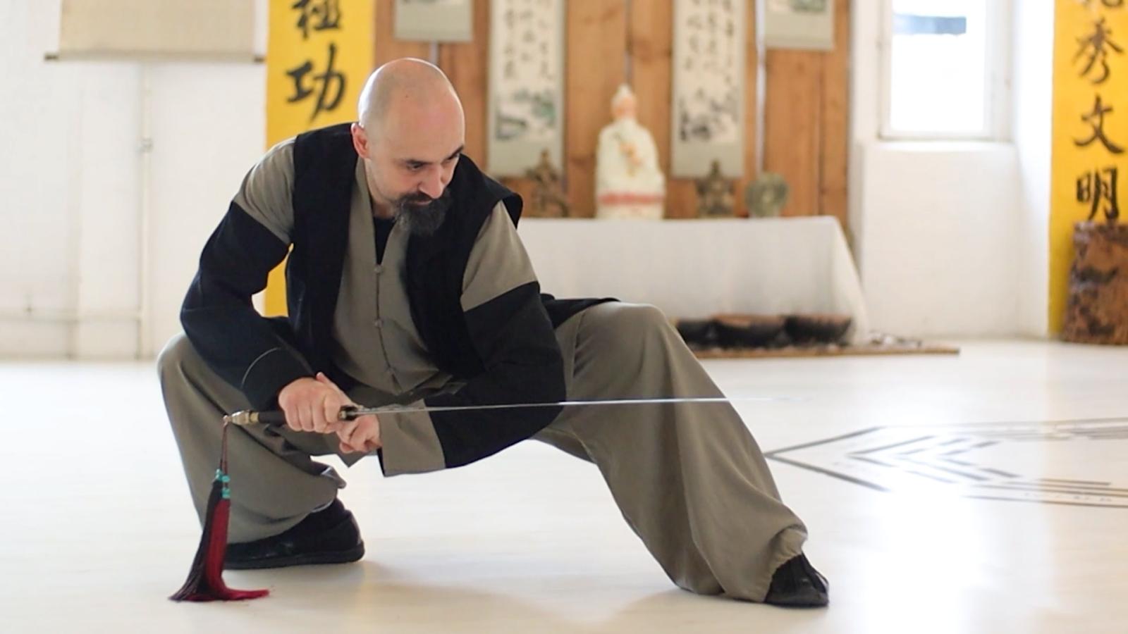 Ismet Himmet demonstrating a low Wudang sword stance (Jian) during indoor training with altar behind.