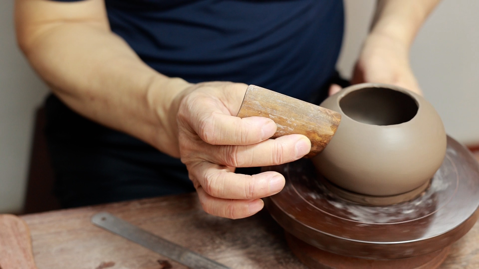 A man using a curved bamboo strip to carefully polish the surface of a Yixing teapot