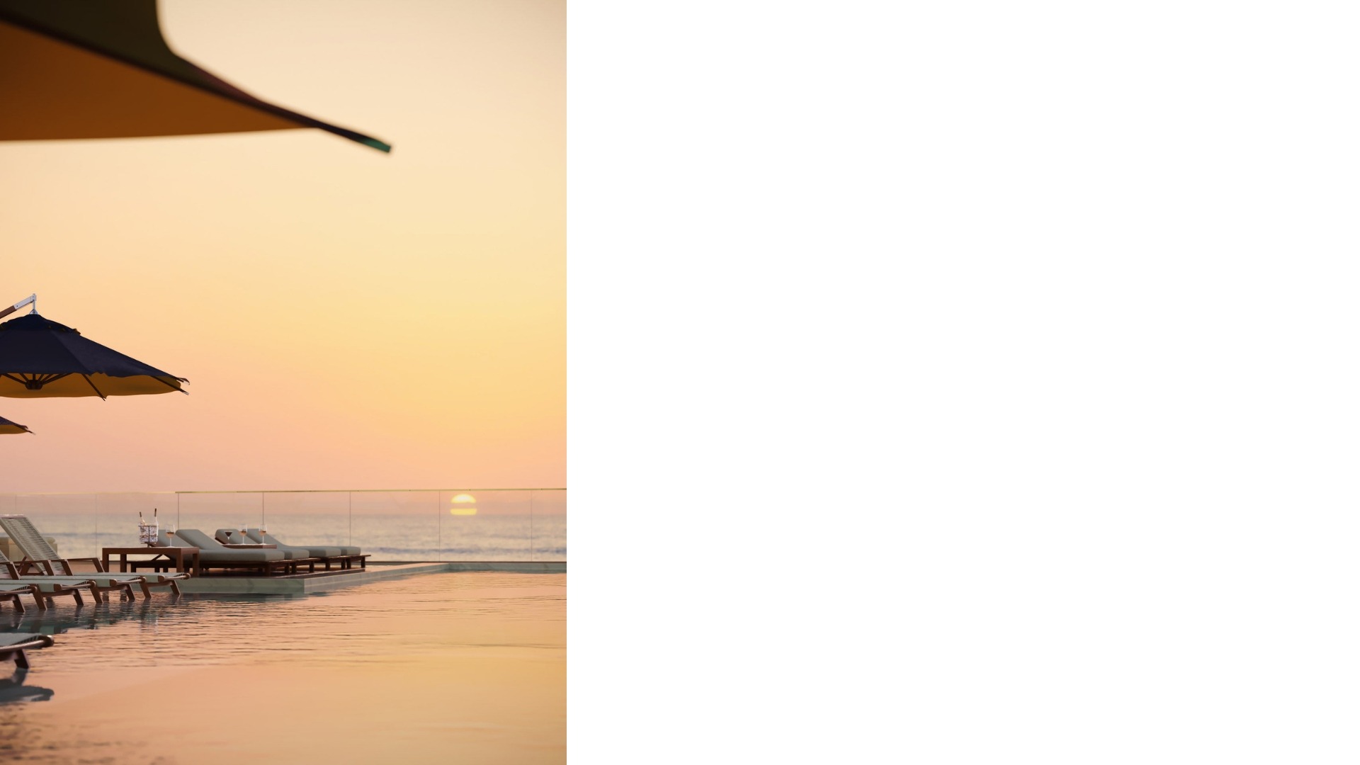 Vista ao nascer do sol, com piscina, cadeiras e guarda-sóis em primeiro plano.