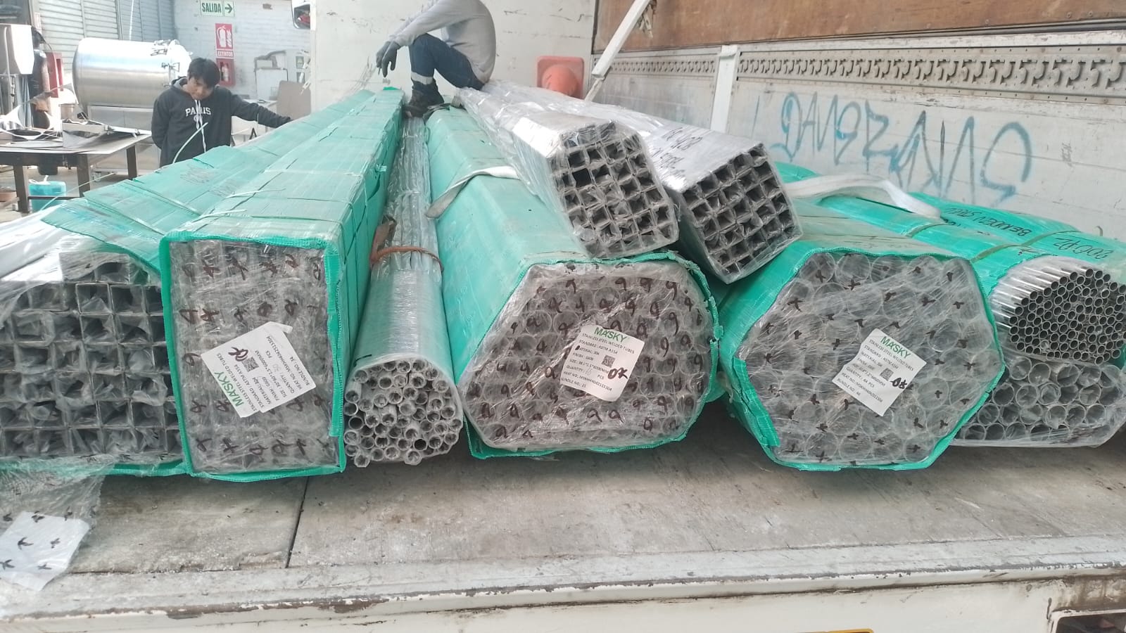 Bundles of stainless steel square and round tubing wrapped in green protective film for industrial delivery.