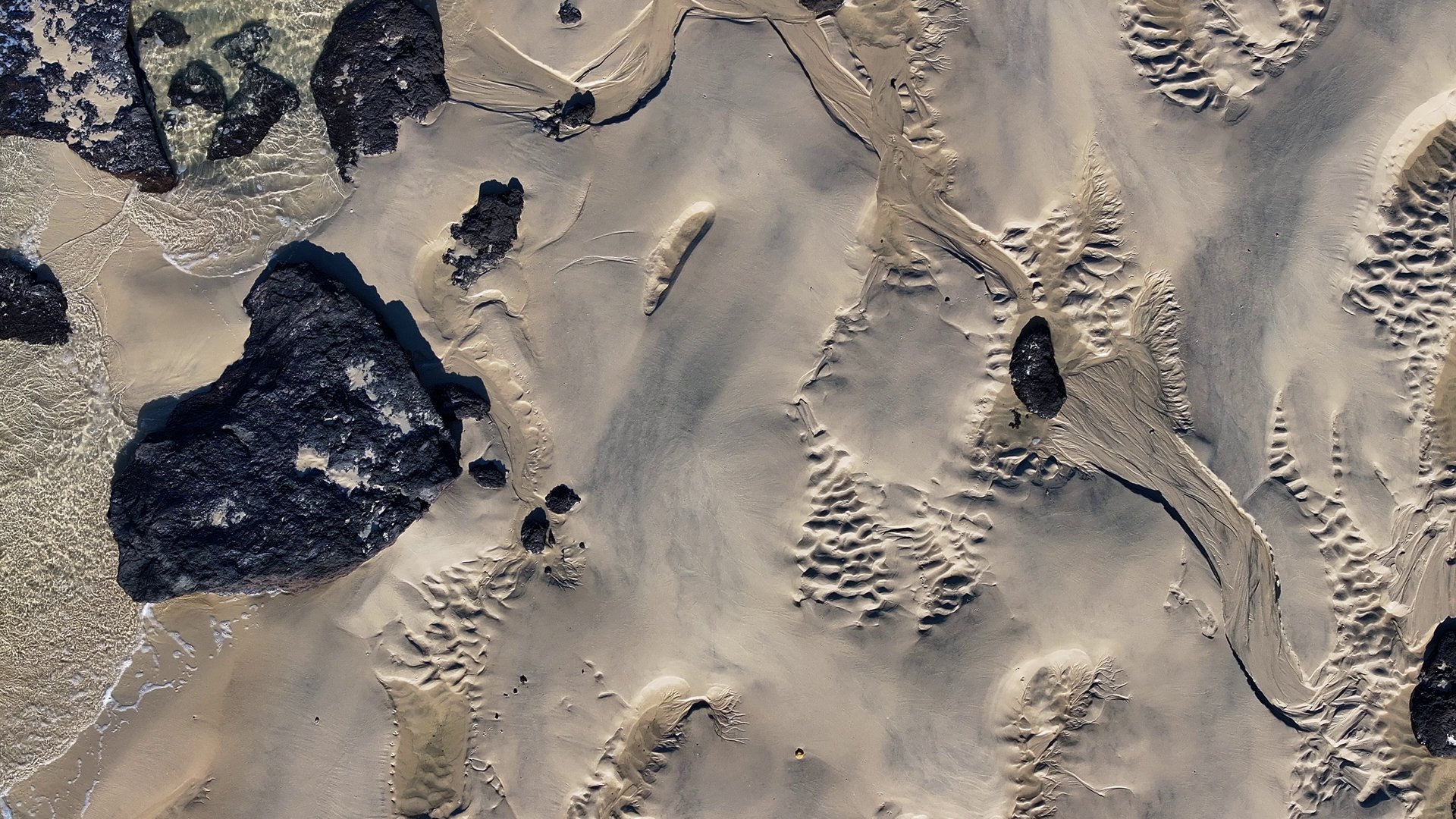 Vue aérienne de motifs de sable de plage texturés avec des roches volcaniques sombres