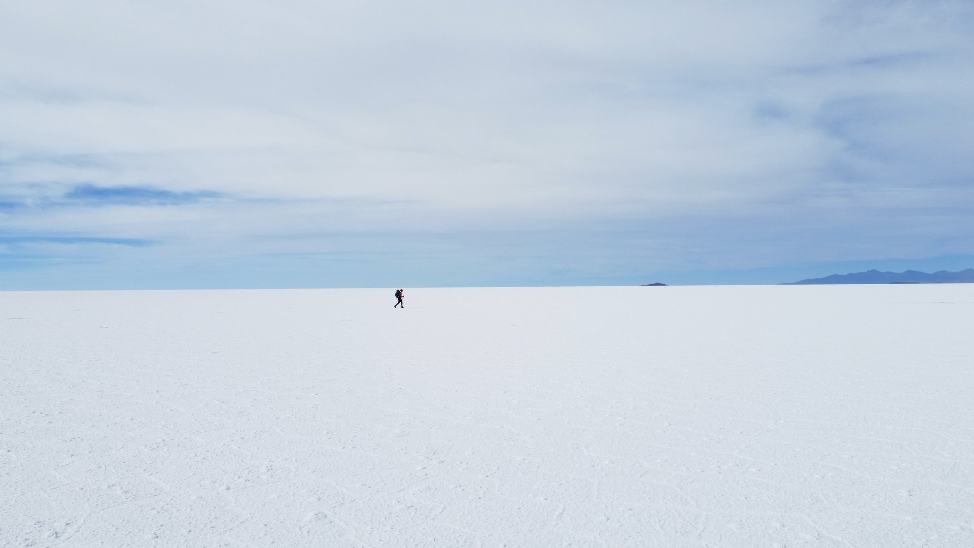 Monsieur Rêve traverse l'immense étendue blanche du Salar d'Uyuni sous un ciel bleu.