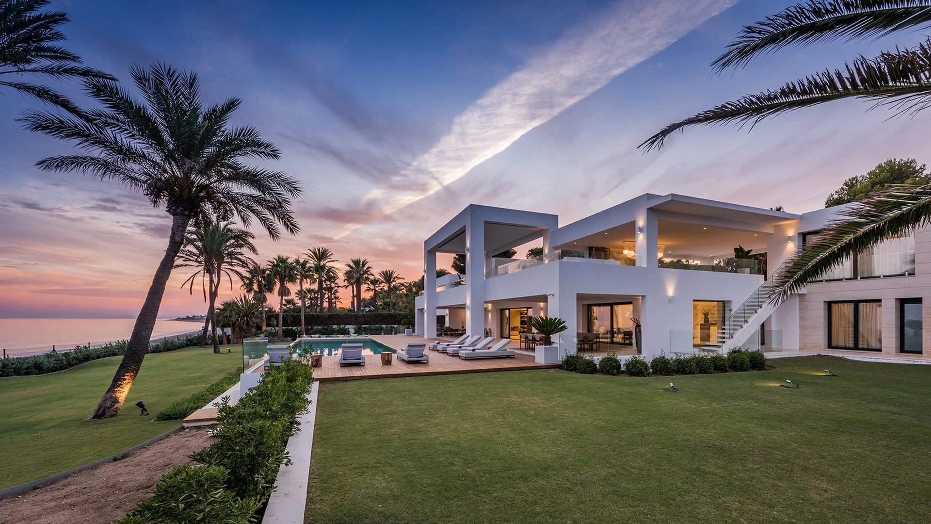 Contemporary beachfront villa at sunset with infinity pool and palm lined gardens