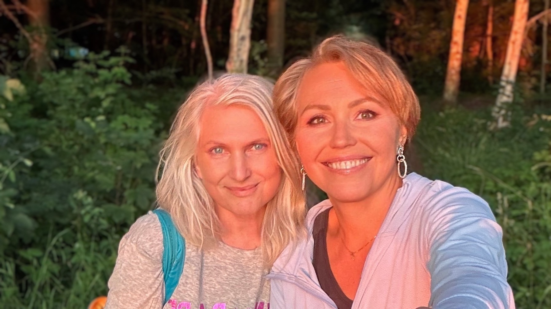 Two smiling women in nature at sunset, glowing with warmth, friendship, and joyful connection.