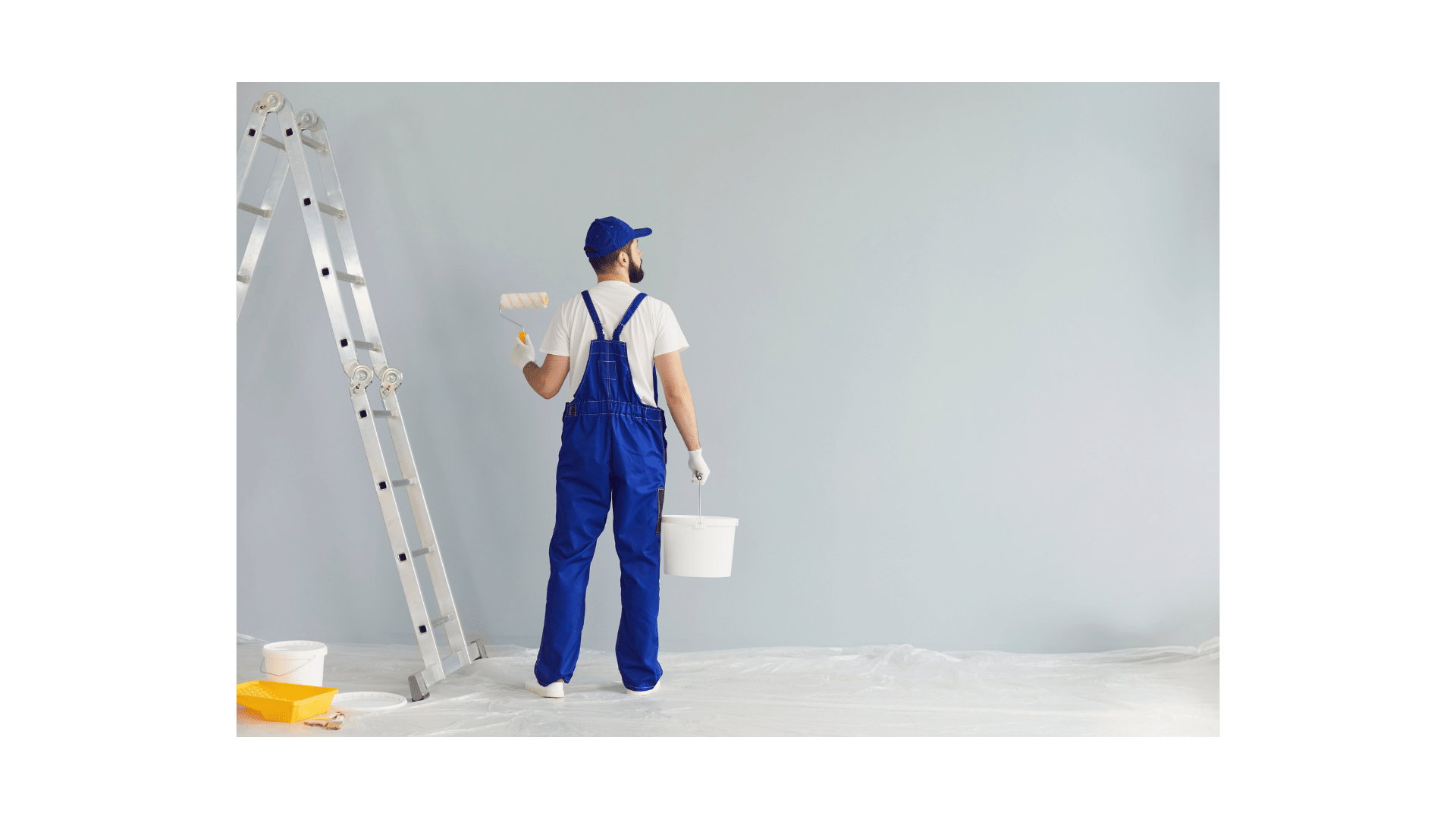 a man in blue overalls and a bucket hat, holding a paint roller