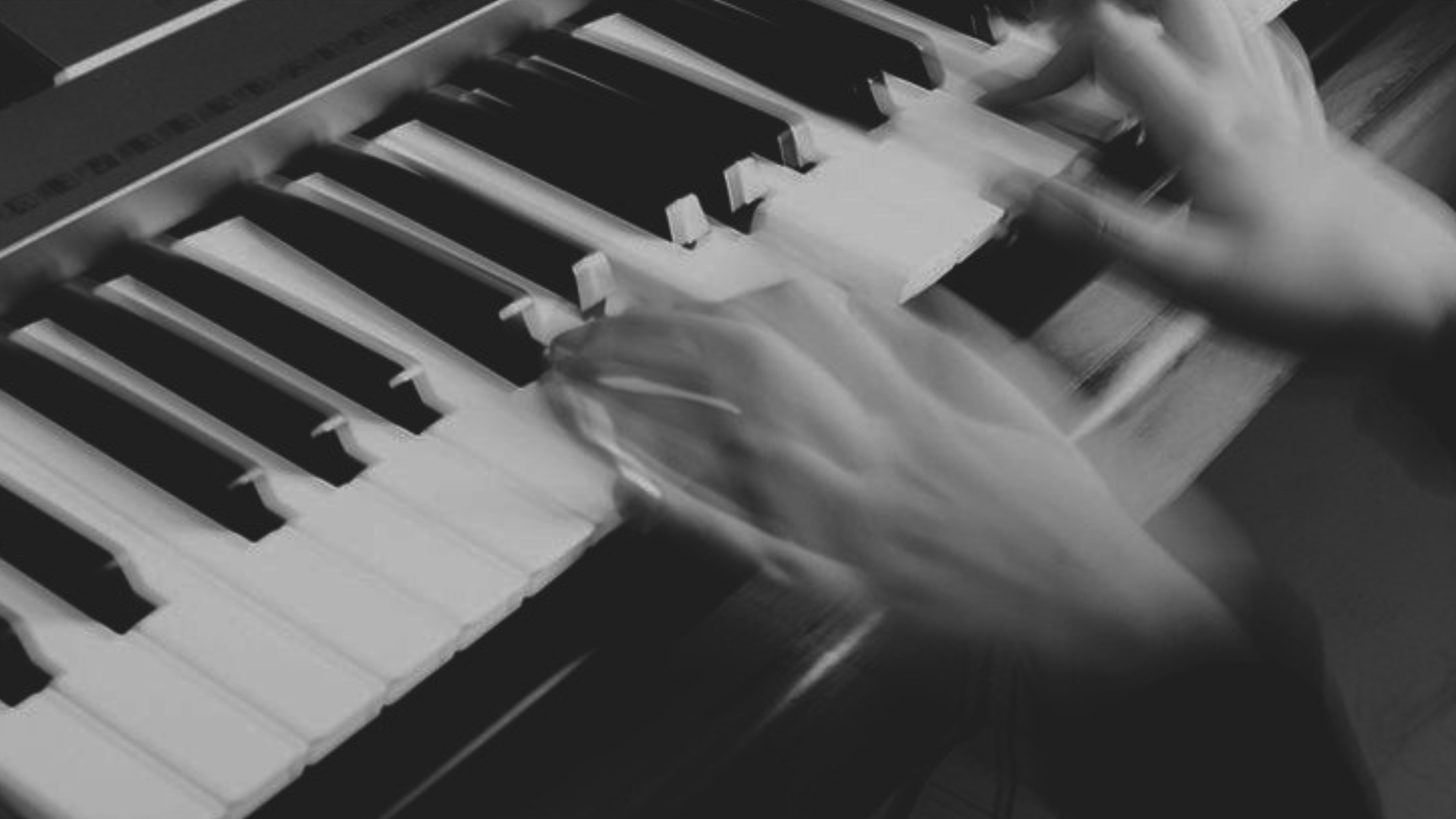 Manos borrosas tocando las teclas de un piano en blanco y negro.