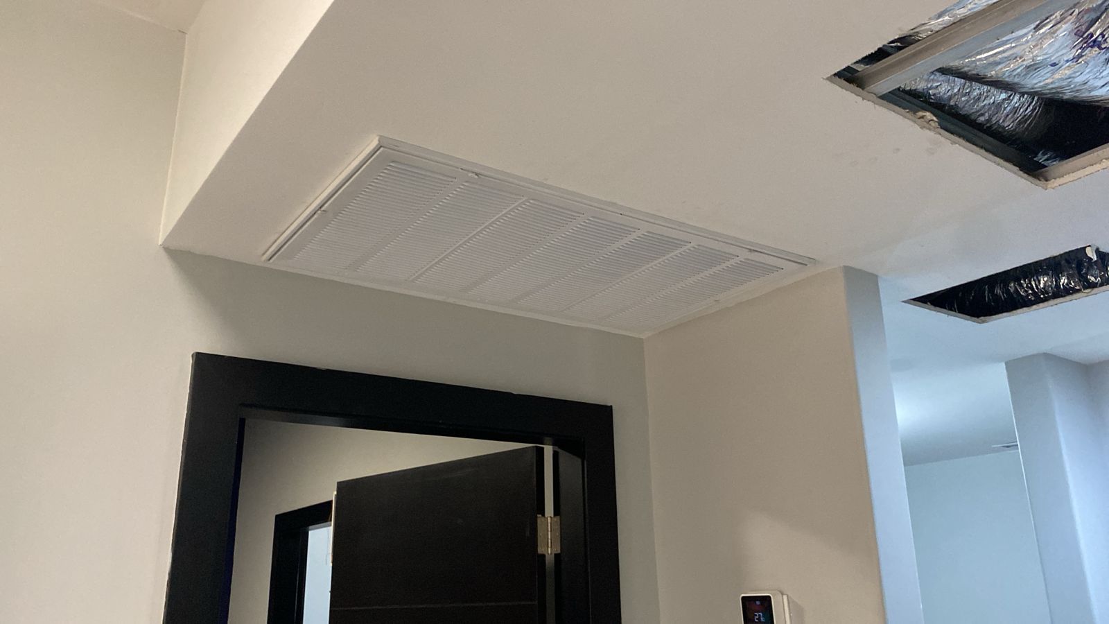 Rejilla de retorno de aire HVAC residencial blanca instalada en un plafón sobre una puerta