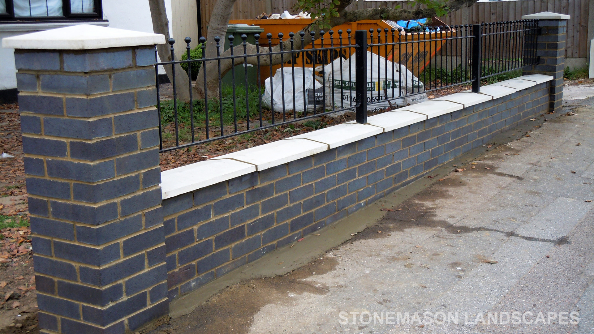 Blue perforated engineering brick wall with white coping, caps and black railings - Romford