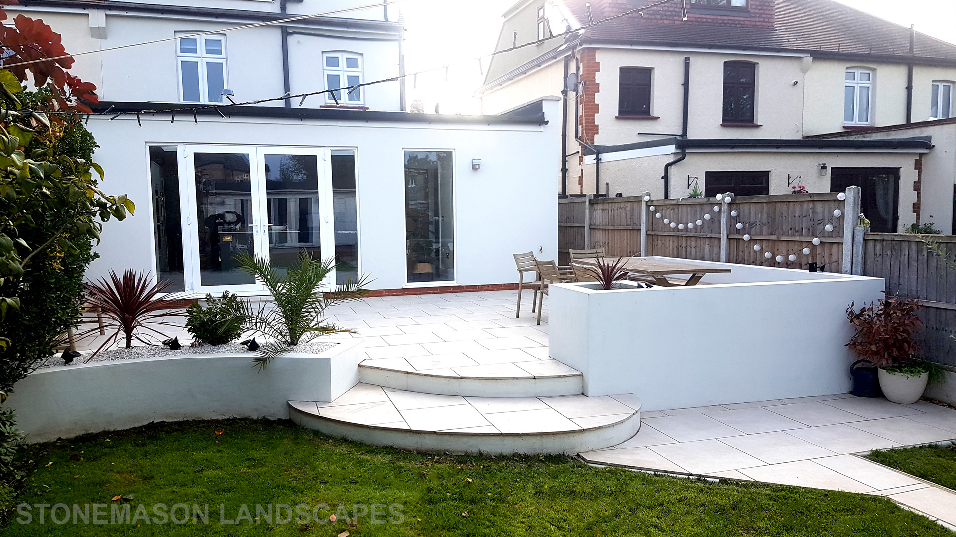 Modern chic raised porcelain patio with white rendered walls and planters