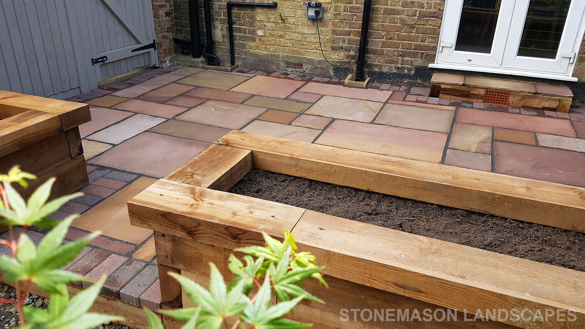 Colourful sandstone patio with raised wooden timber planter seating
