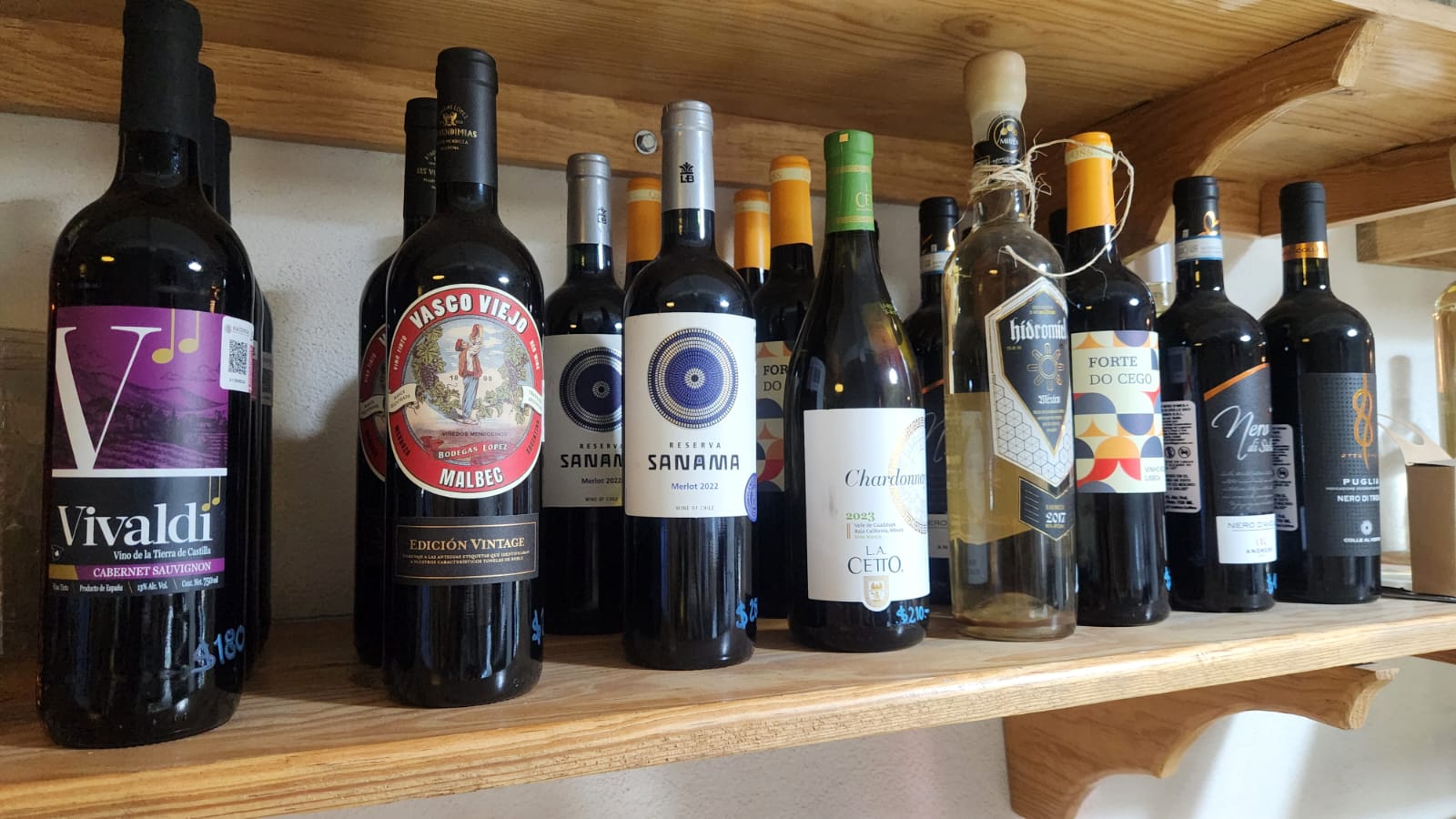 A collection of red and white wine bottles, including Malbec and Chardonnay, on a rustic wooden shelf.
