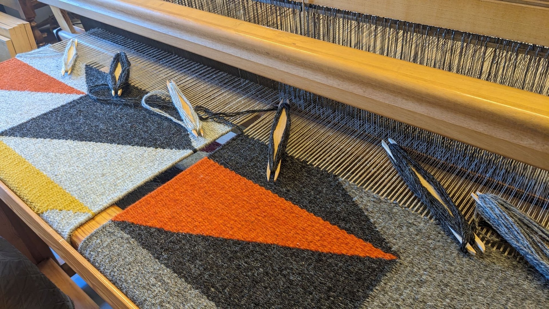 a weaving loom with shuttles and gray orange yellow black wool threads on a kilim rug in progress