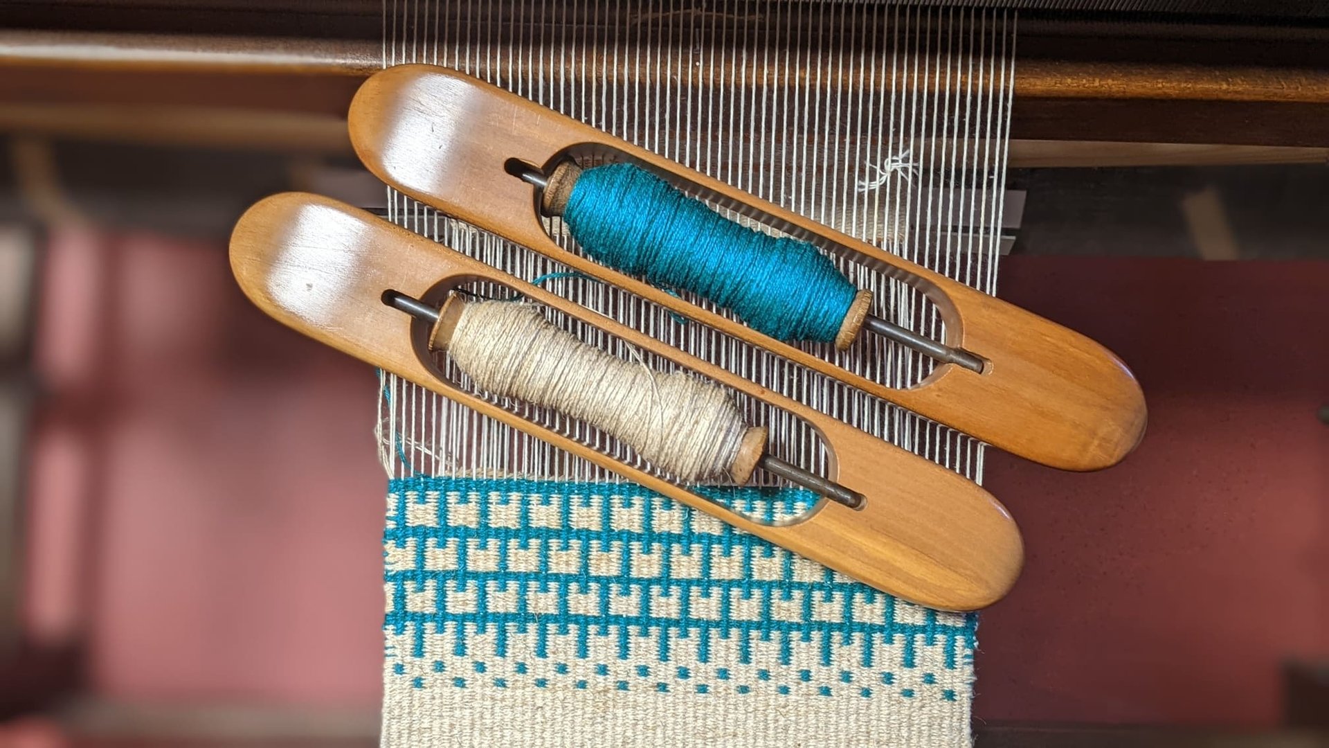 Blue and white krokbragd weaving is currently being done on a weaving loom with wooden shuttles and 