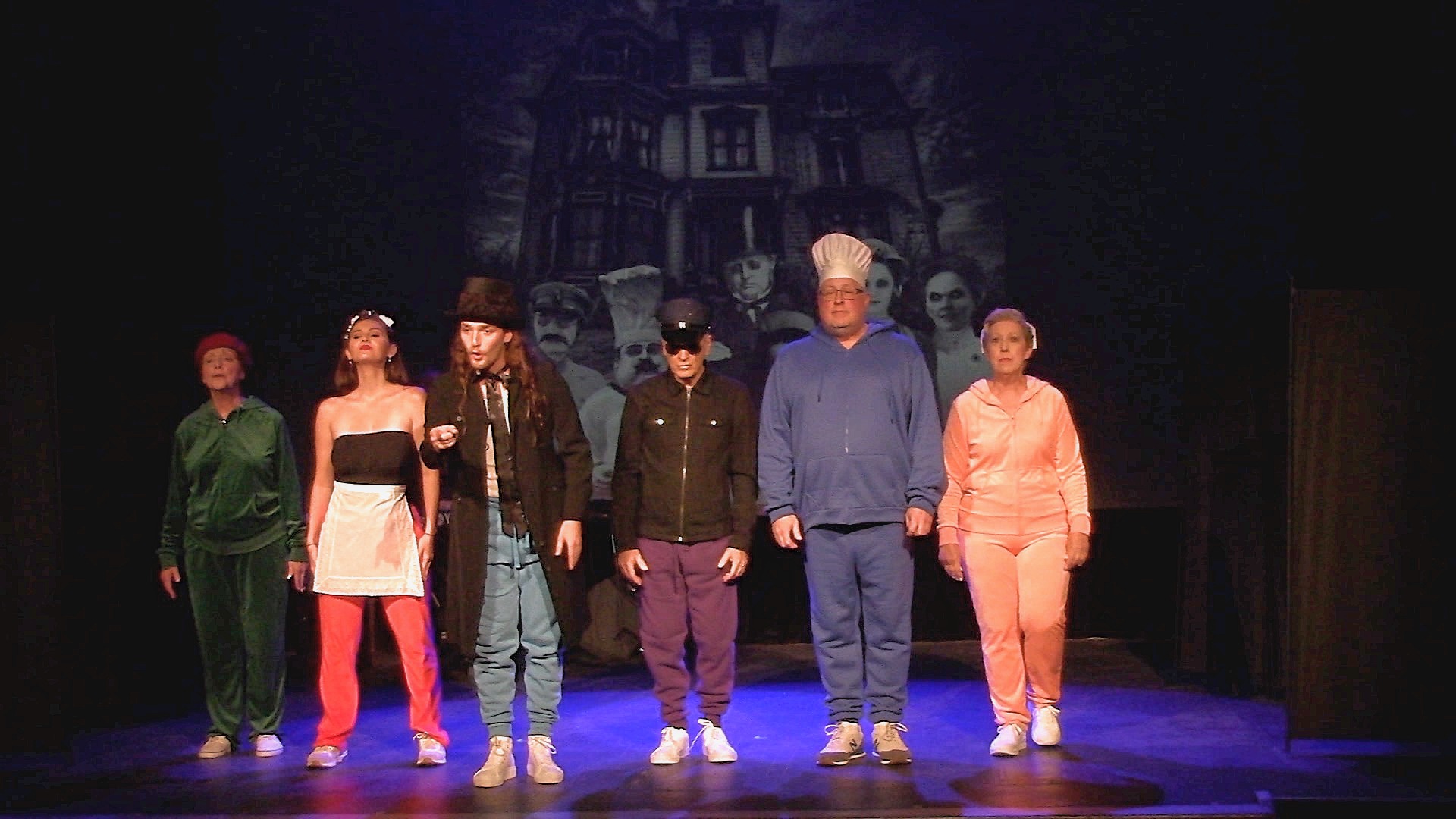 Actors in colorful costumes a musical number in front of a haunted house backdrop.