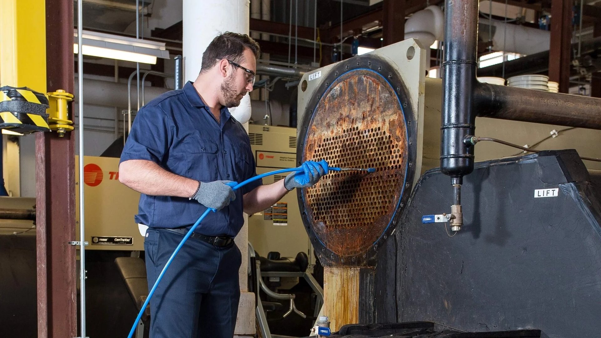 An HVAC technician performs maintenance by cleaning industrial chiller condenser tubes.