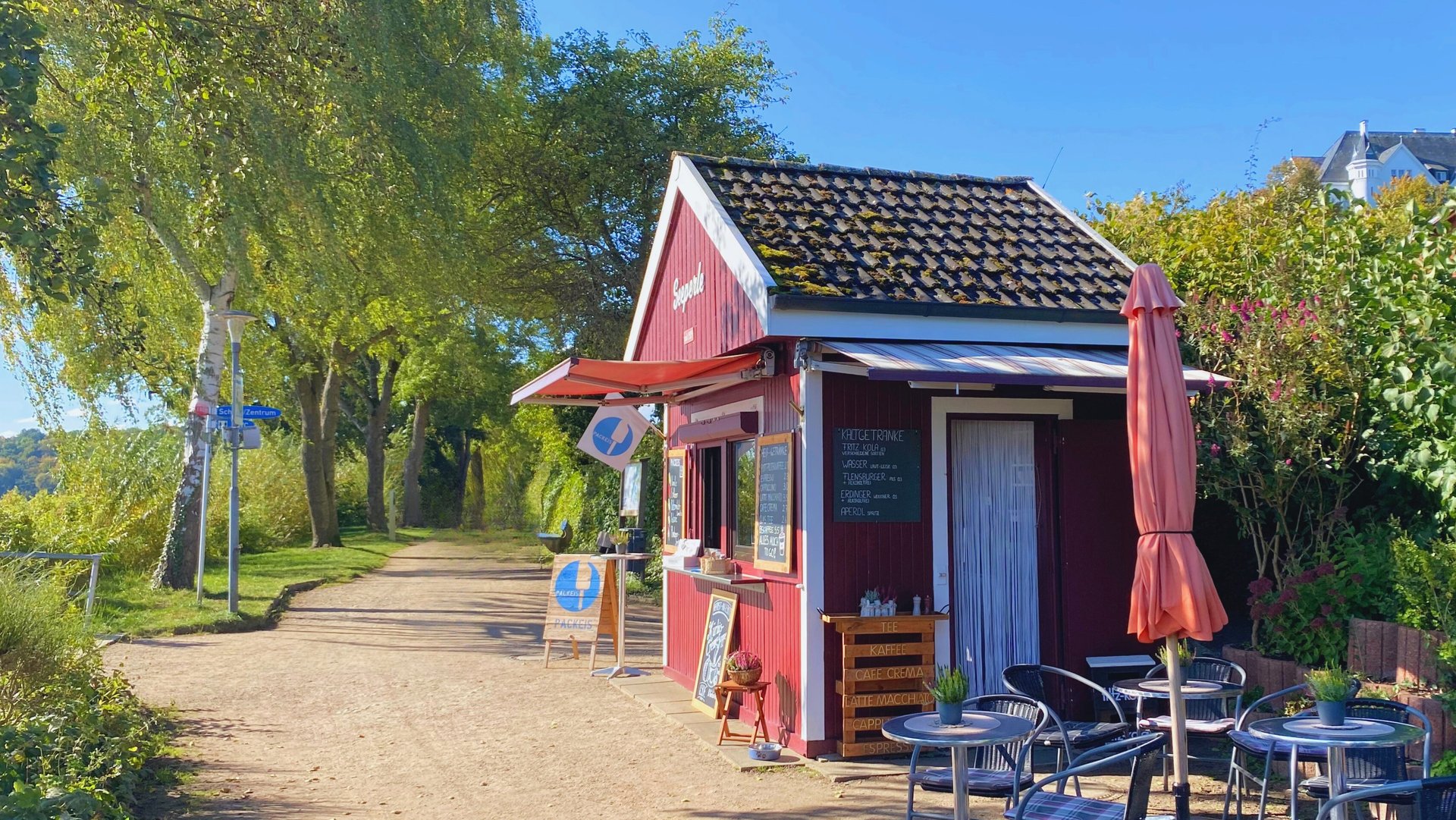Der kleine Imbiss "Seeperle" am Plöner See mit Sonnenschein und Blick auf den Wanderweg