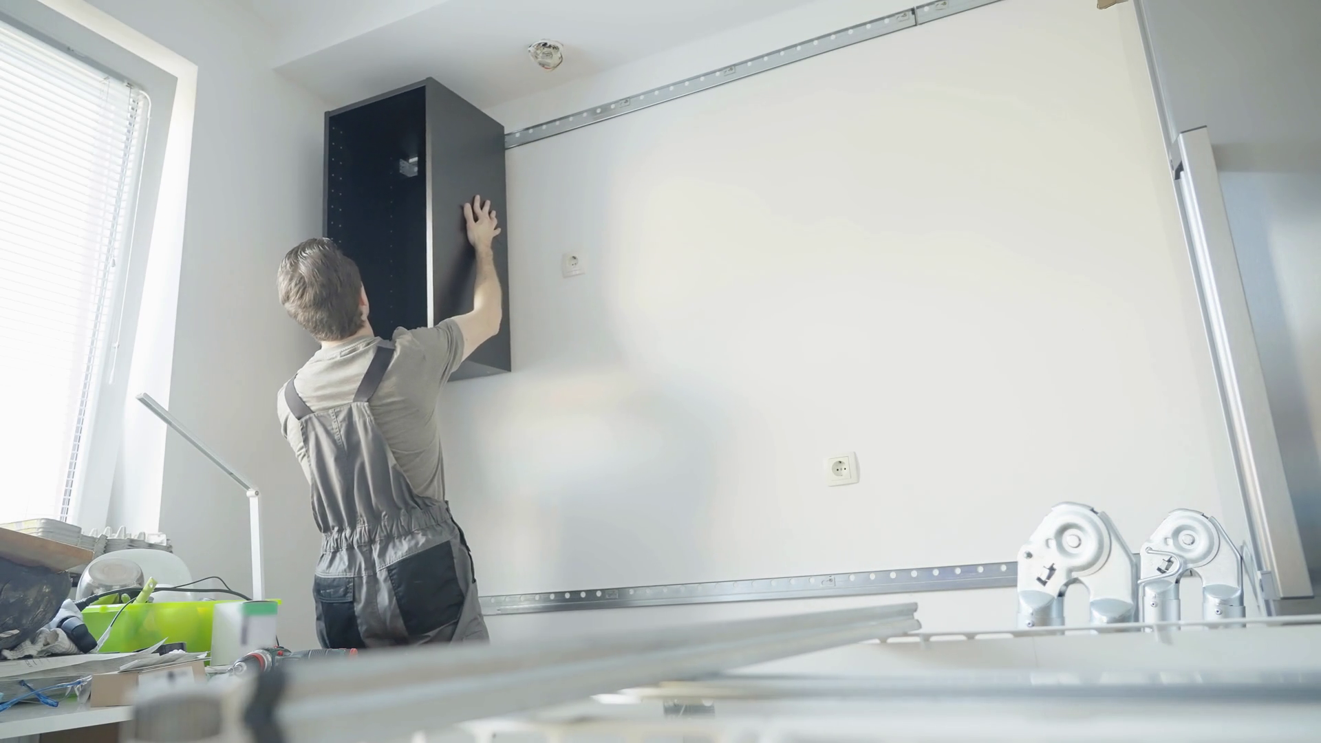 Mężczyzna montuje korpus szafki wiszącej za pomocą listwy montażowej 