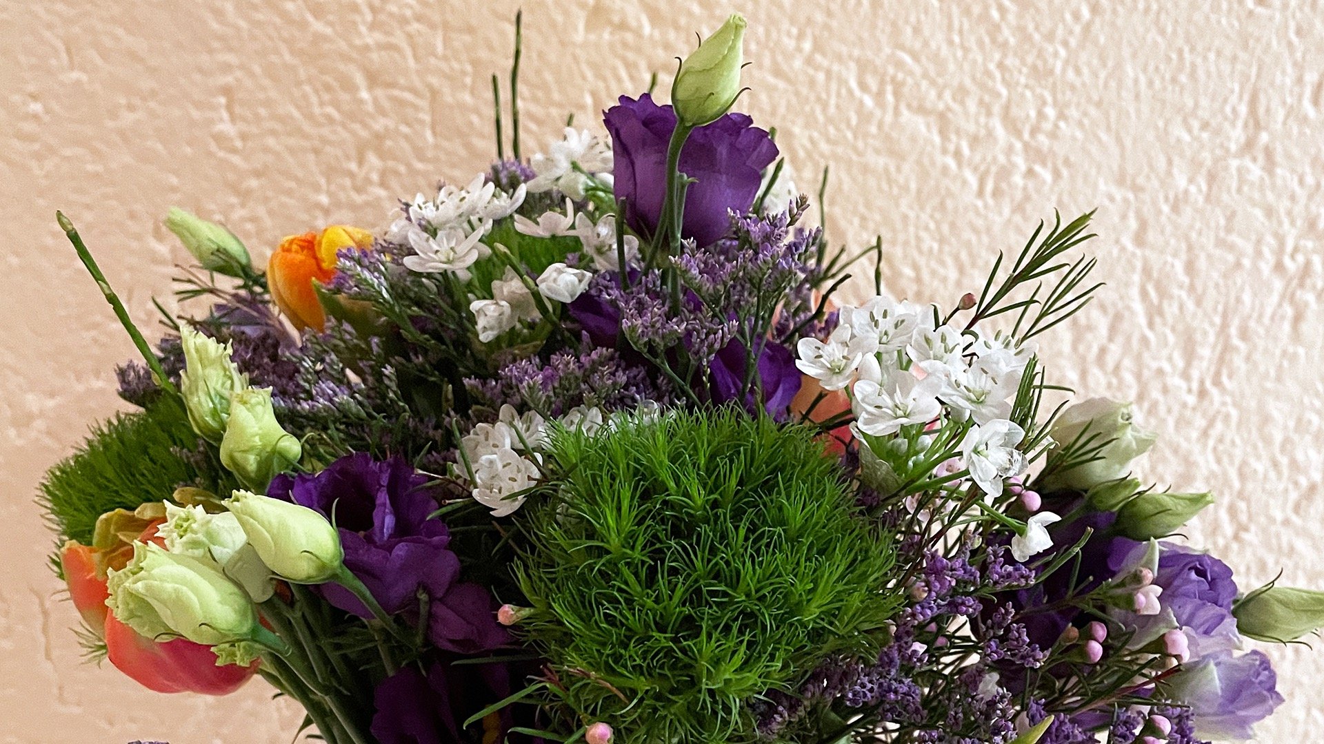 A colorful flower bouquet featuring purple lisianthus, white fillers, and green dianthus.