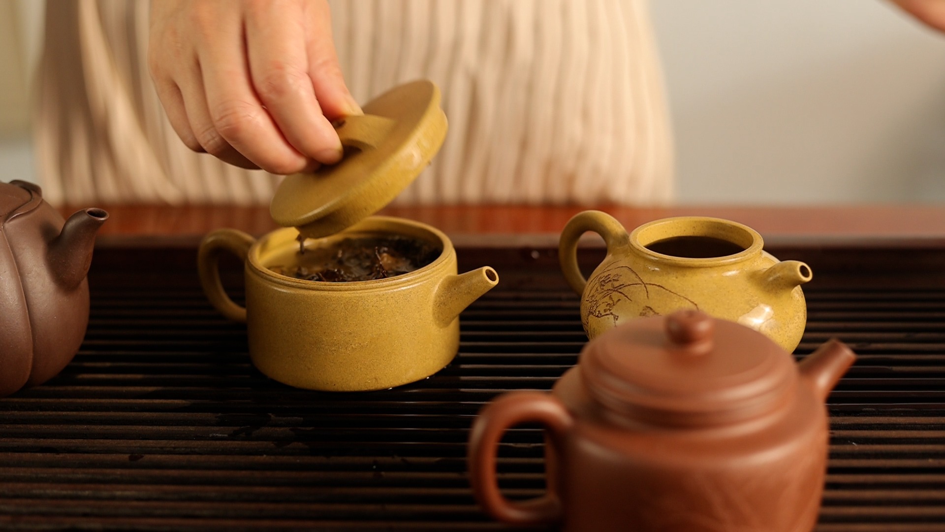 A hand lifting the lid off a teapot, revealing tea inside