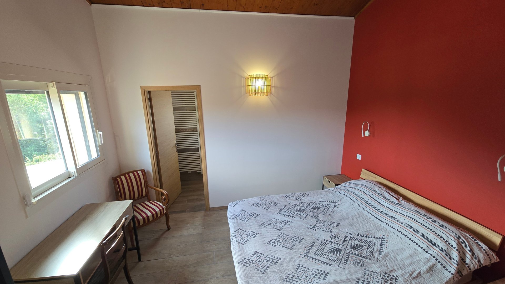 Vue de la chambre d'hôtes depuis la porte d'entrée, avec lit double, bureau et chaise.
