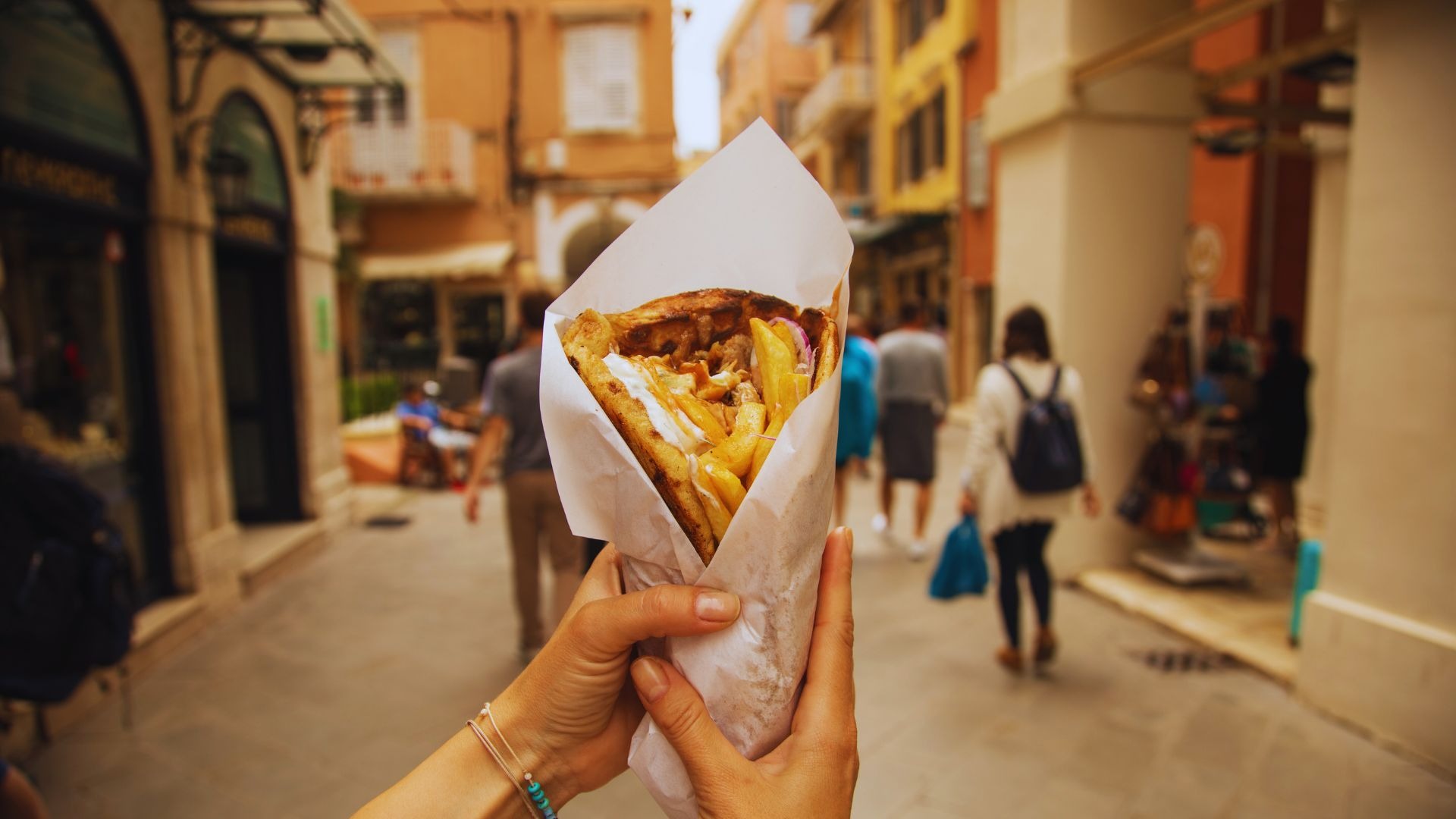Autora segurando um gyros enquanto caminha pelas ruelas movimentadas de Corfu, explorando a cidade.