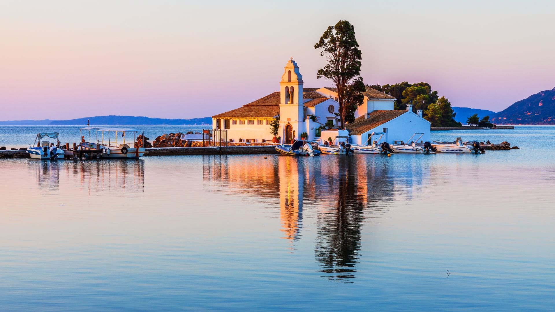 Vista do passeio de barco em Corfu, com a igreja no mar ao fundo e barcos ancorados no pier.