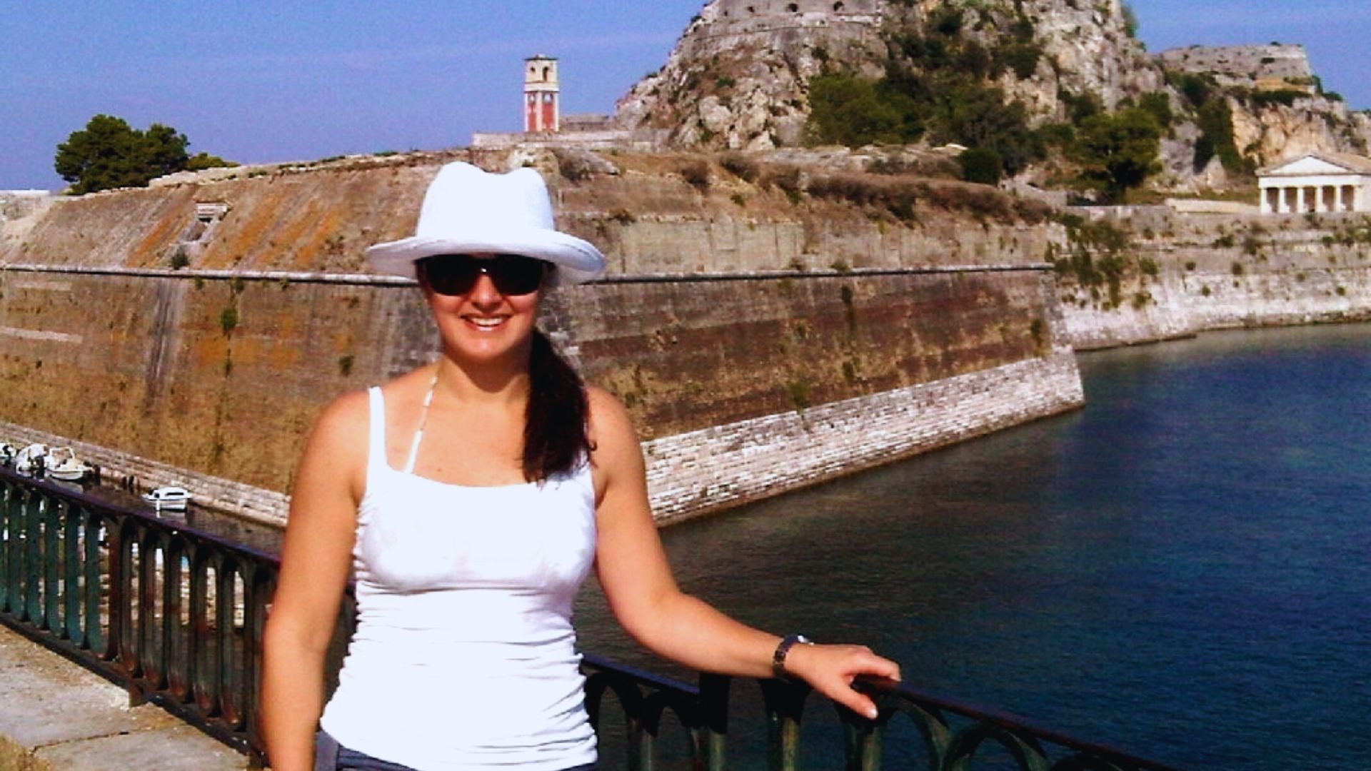 Autora diante da Fortaleza Antiga de Corfu, com a imponente estrutura histórica ao fundo.