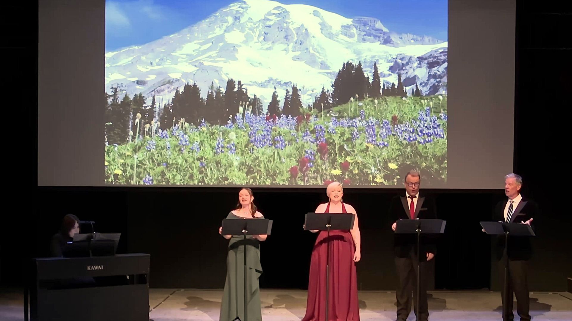 Two female & two male vocalists singing against a mountain & wildflower meadow backdrop