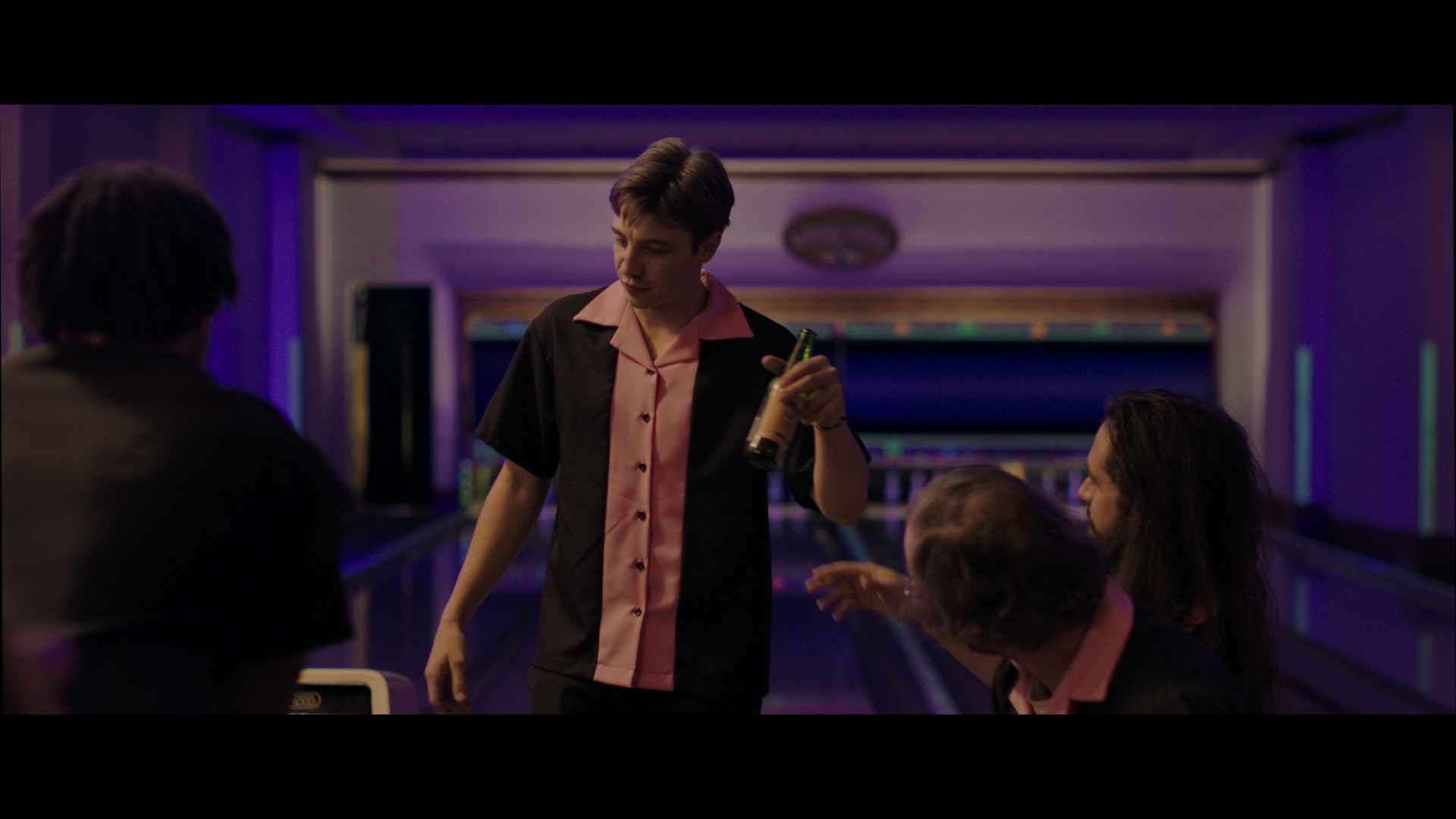 a man in a bowling shirt is holding a bottle of beer