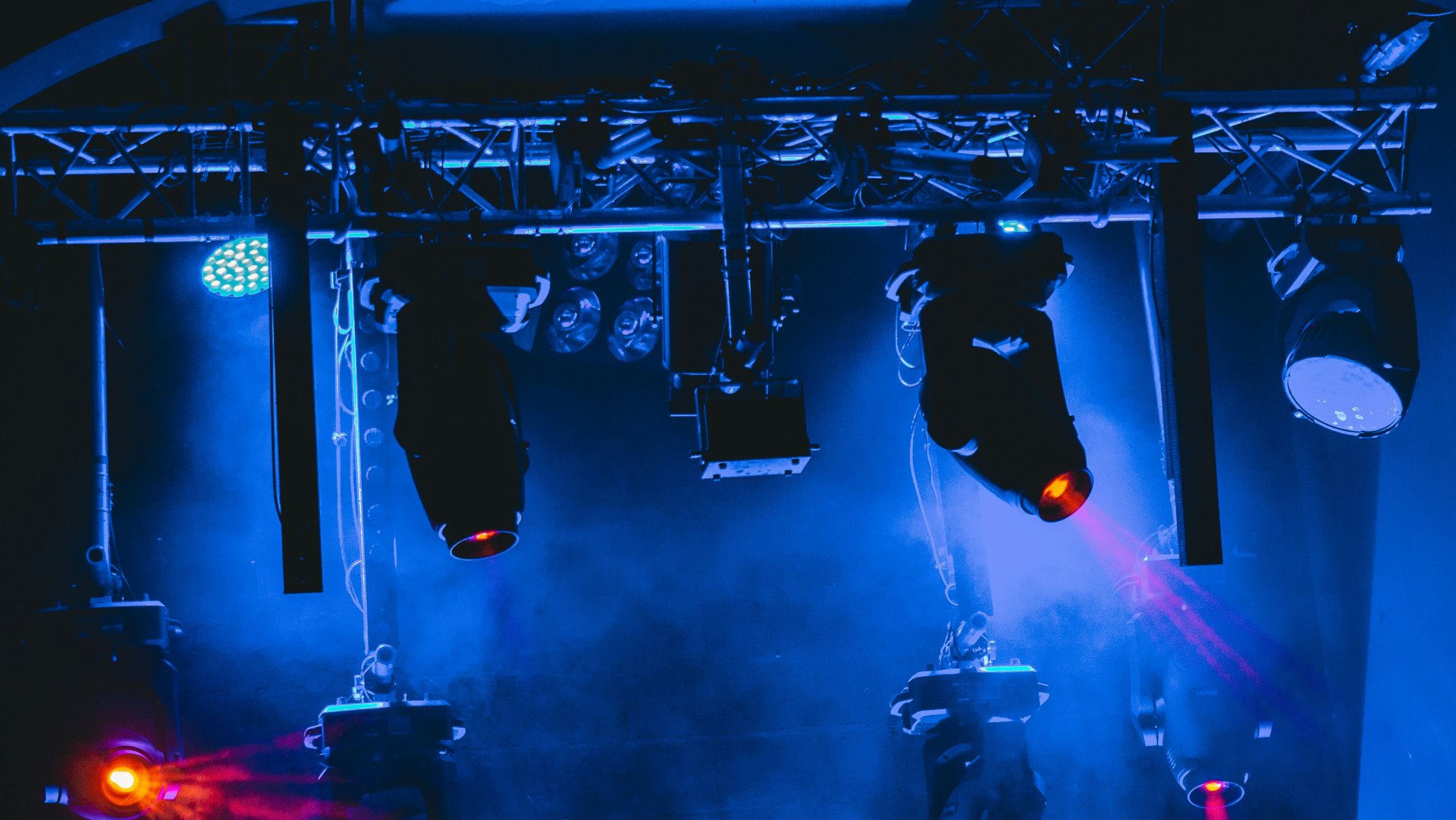 Professional stage lighting rig with spotlights and blue atmospheric haze for a concert event.