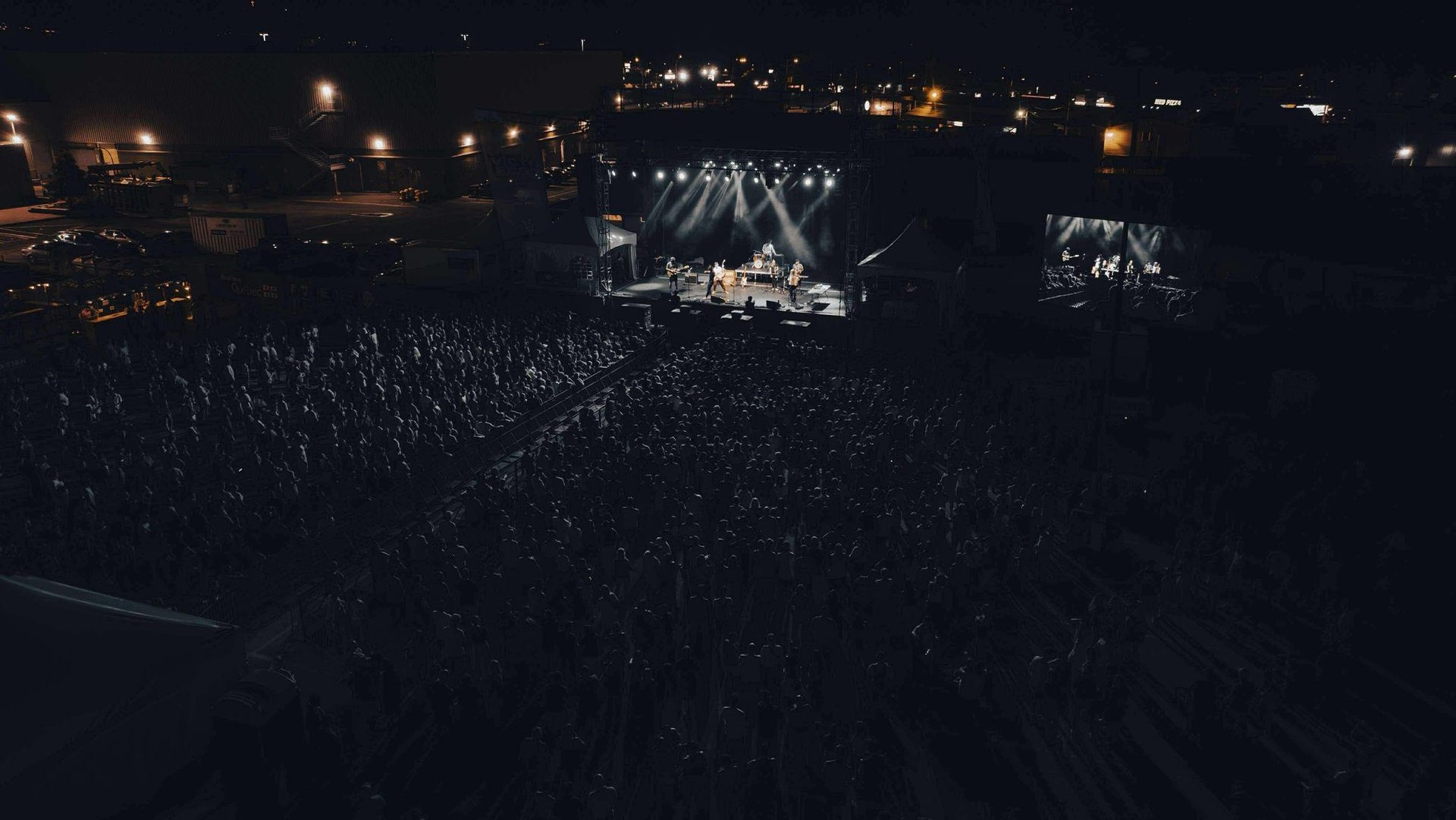 A live outdoor music concert at night with a large crowd gathered before a brightly lit stage.