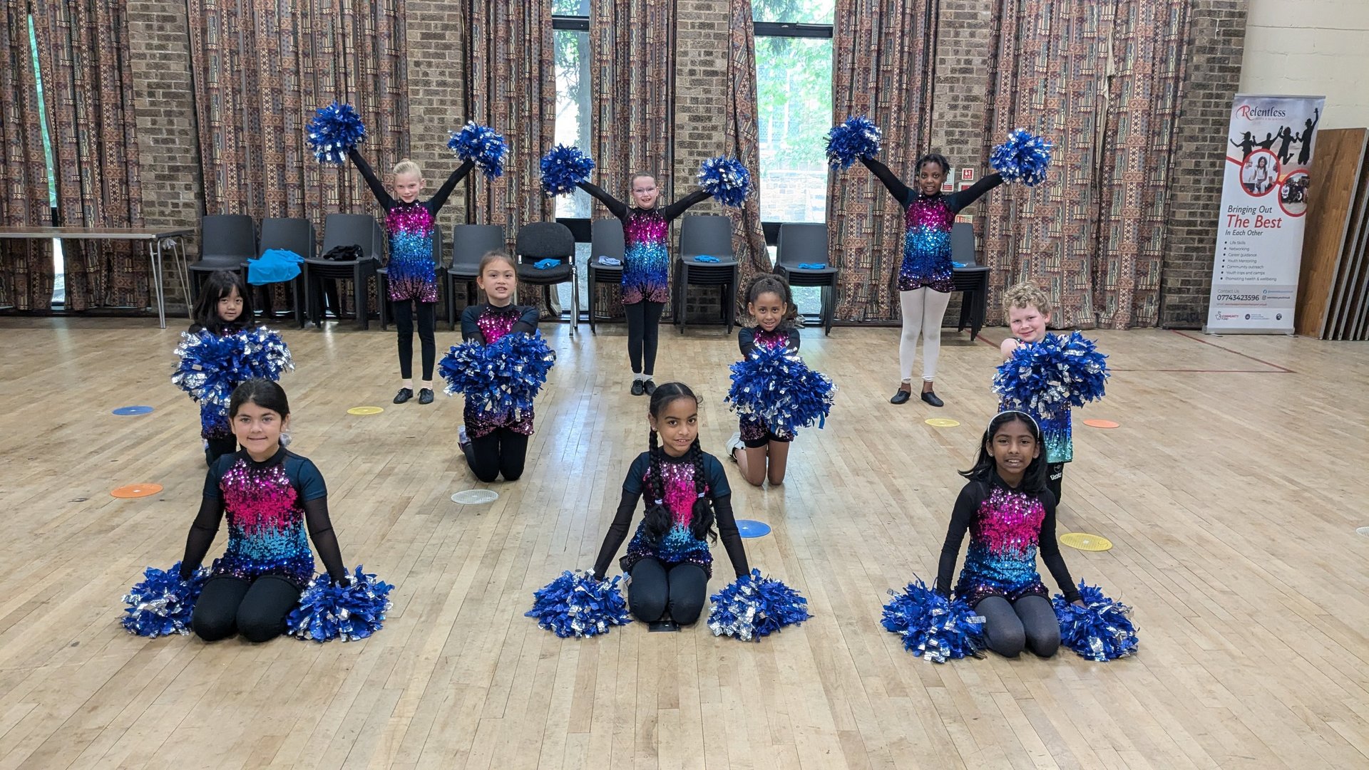 Young cheerleaders in sequined uniforms posing with blue pom poms during a dance class performance.