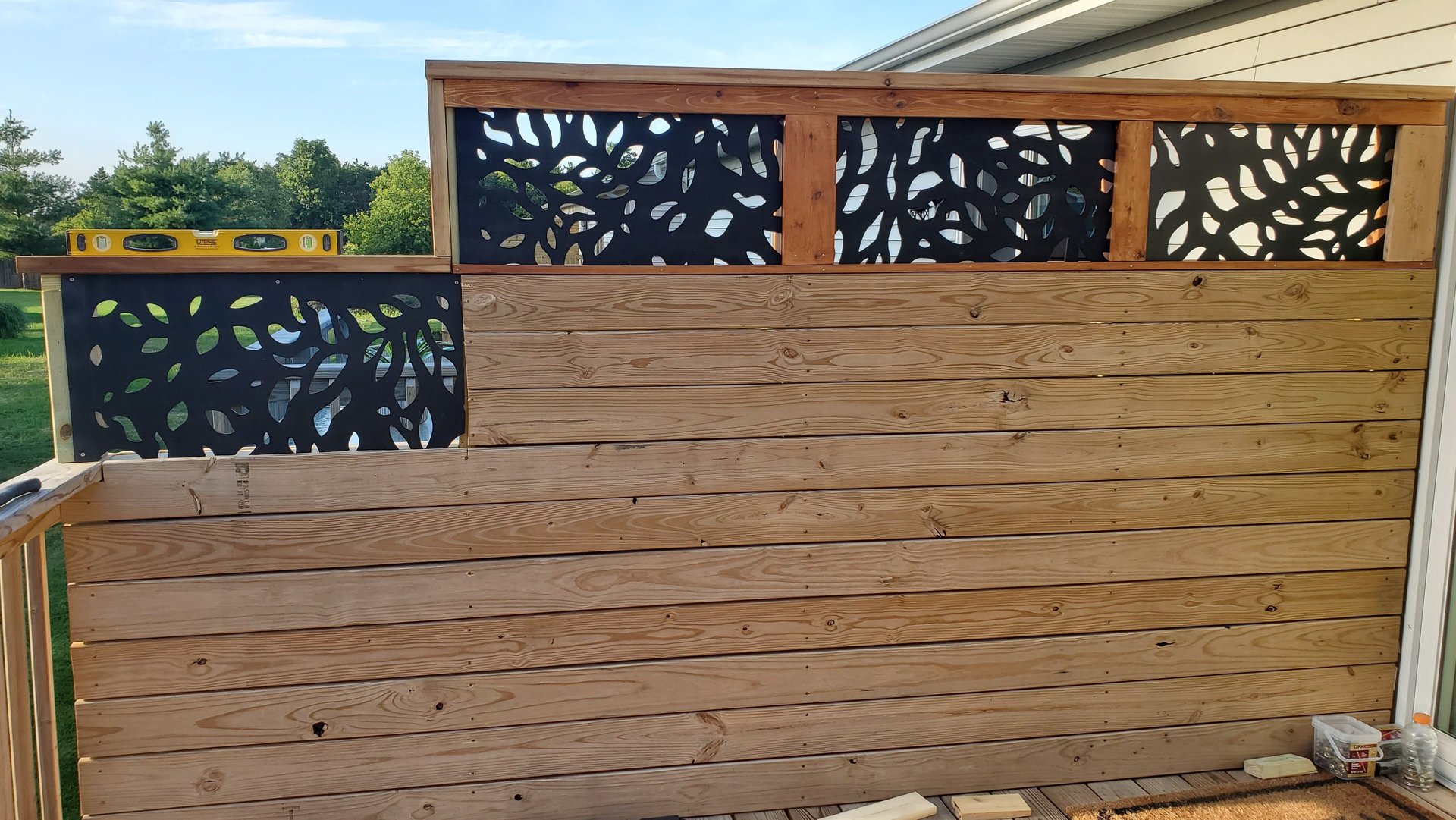 Custom wood privacy fence with decorative black laser-cut metal screens on a backyard deck.